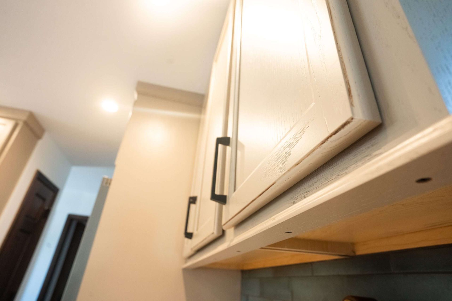 Close-up of light wood kitchen cabinets with black handles and ceiling lights in a hallway.