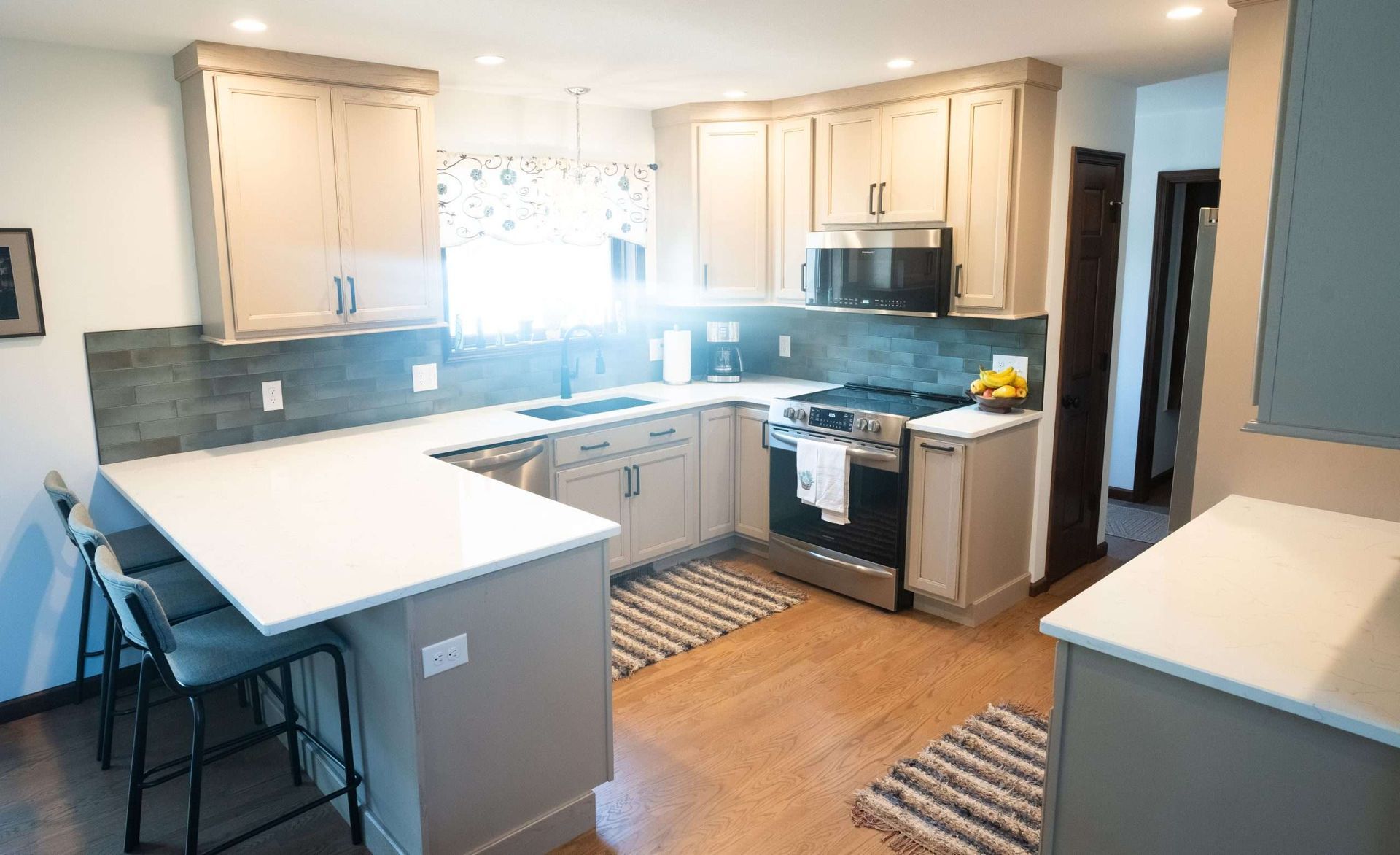 Bright kitchen with white cabinets, blue backsplash, island, bar stools, and stainless steel appliances