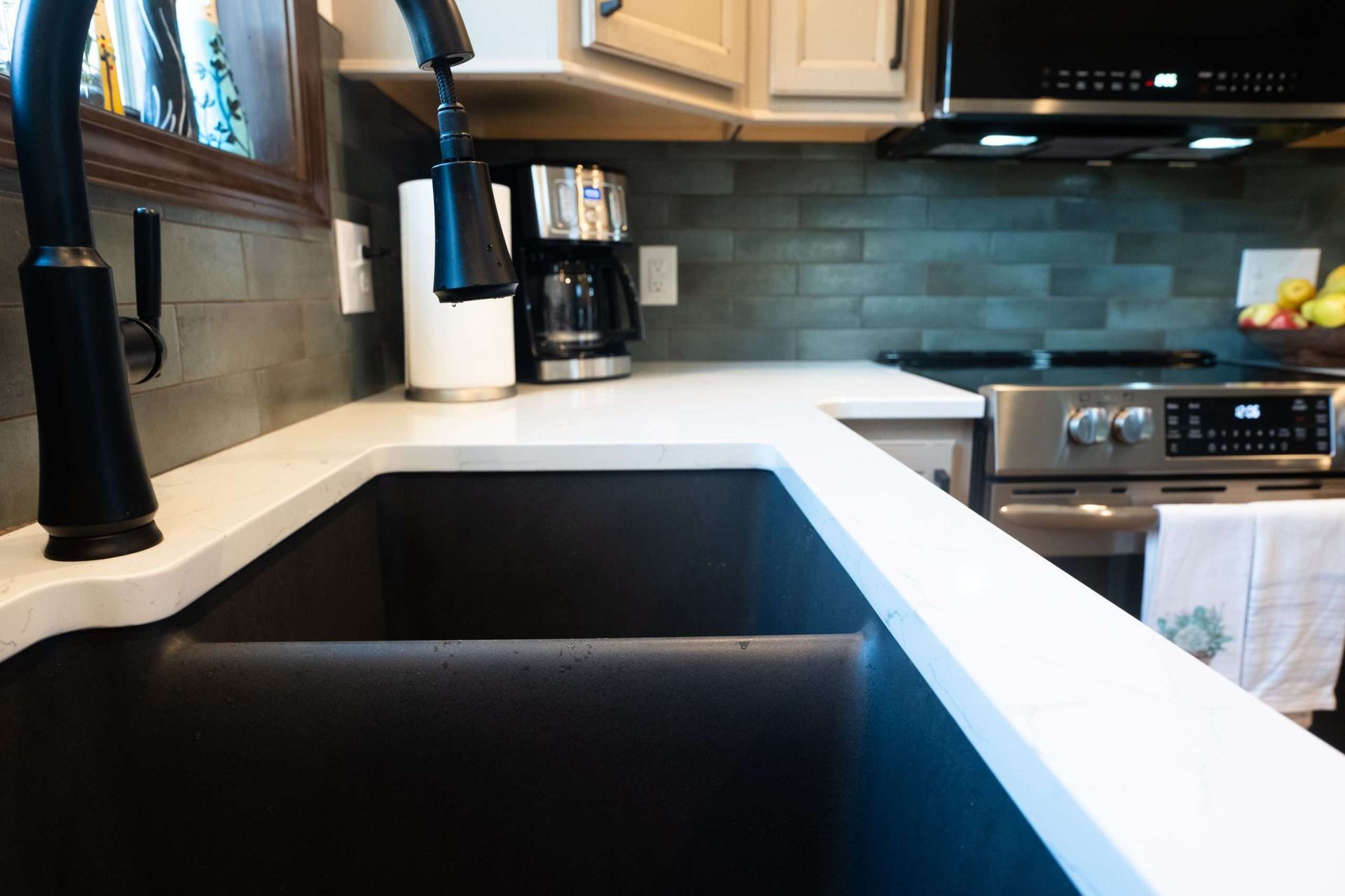 Modern kitchen with black sink, white countertops, beige cabinets, and stainless steel appliances.