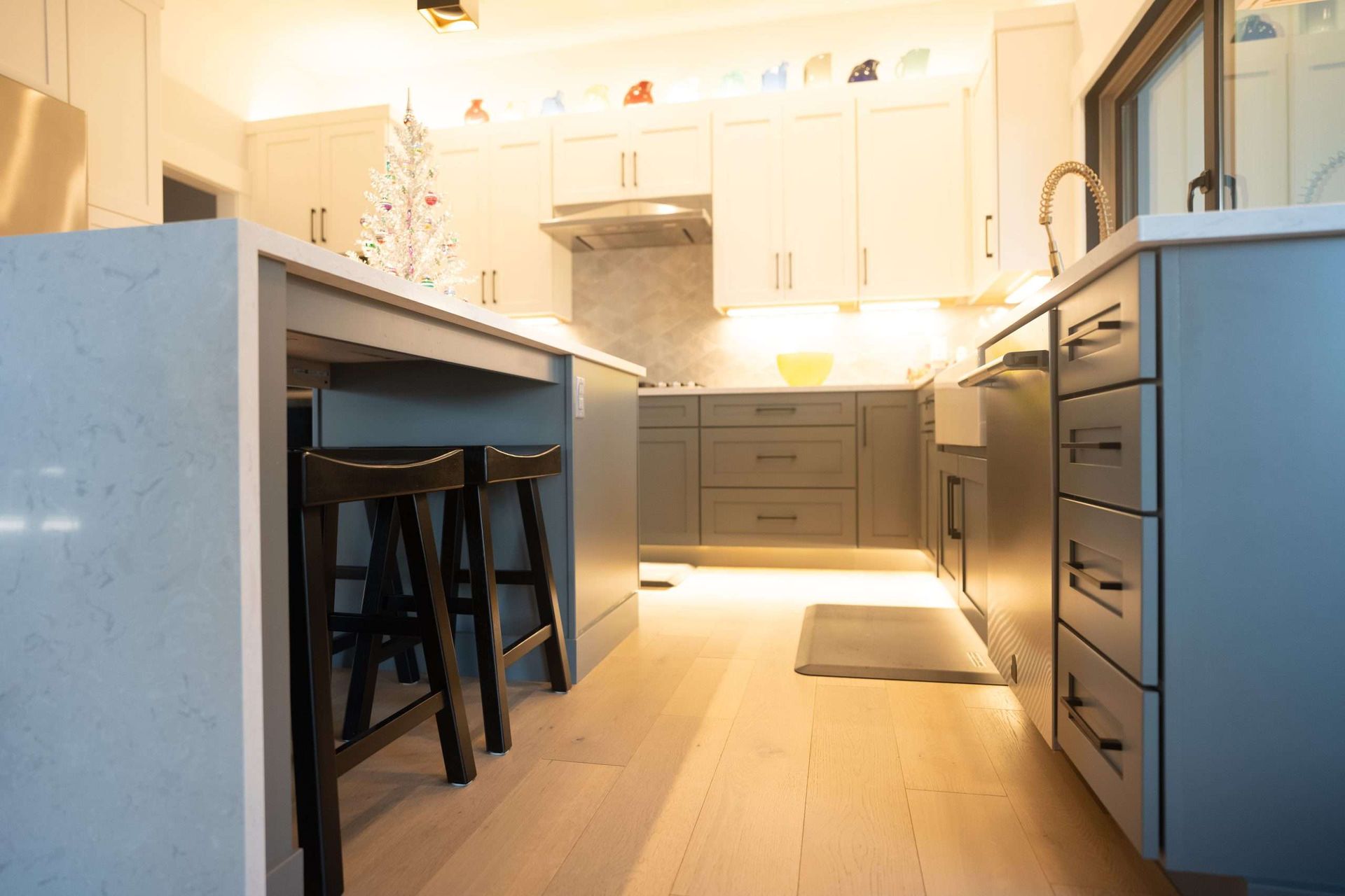 Modern white kitchen with island, bar stools, stainless range hood, and gray drawers