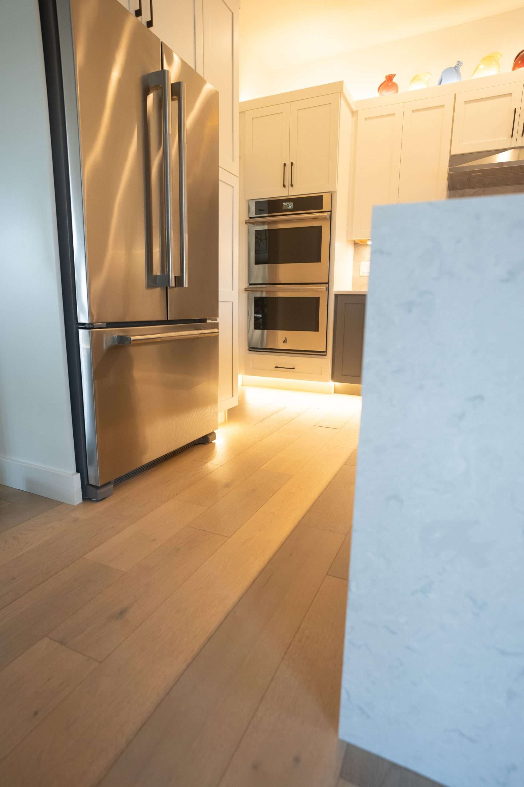 Bright kitchen with stainless steel fridge, built-in ovens, and light wood floors.