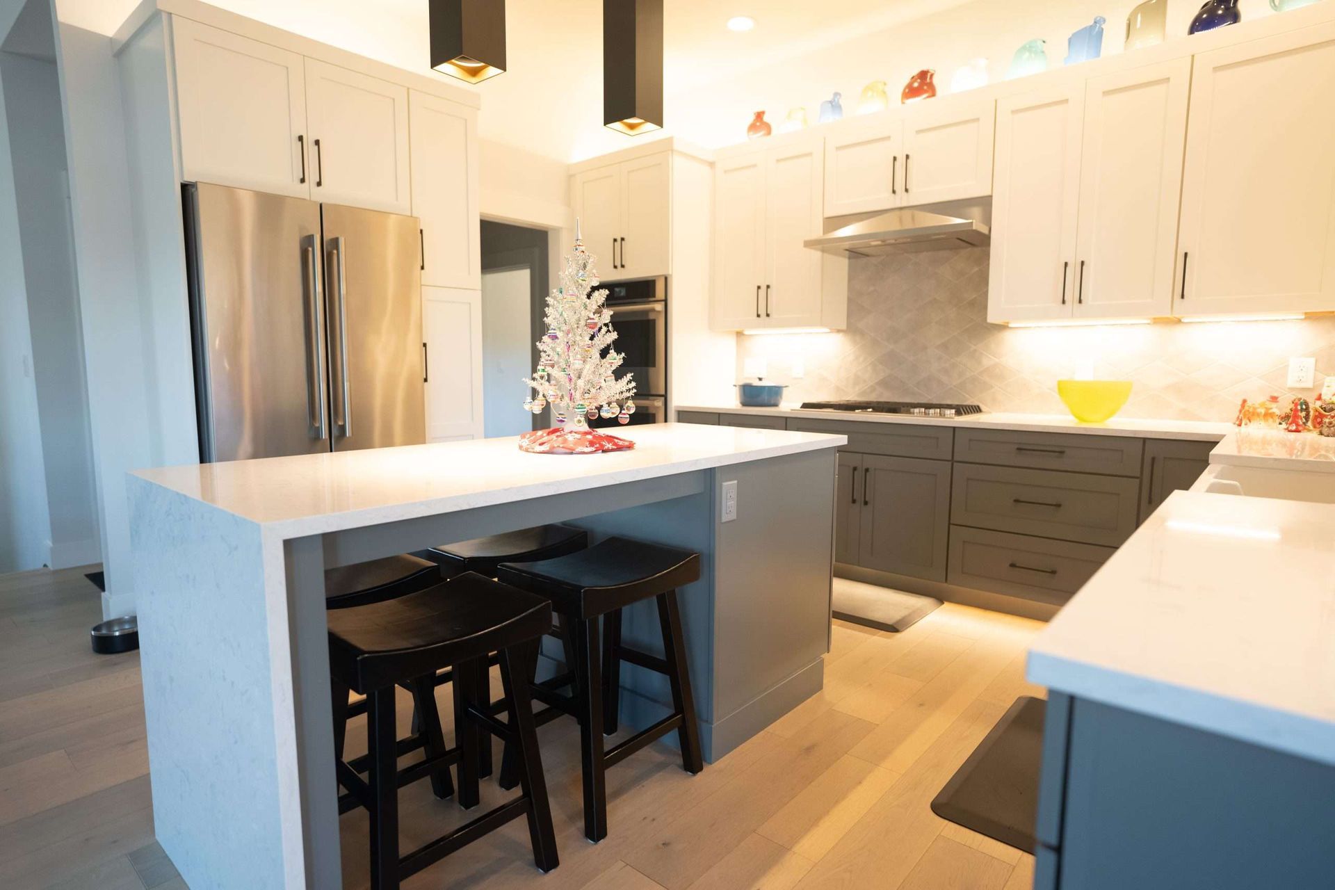 Bright modern kitchen with white cabinets, gray island, stainless fridge, and black stools