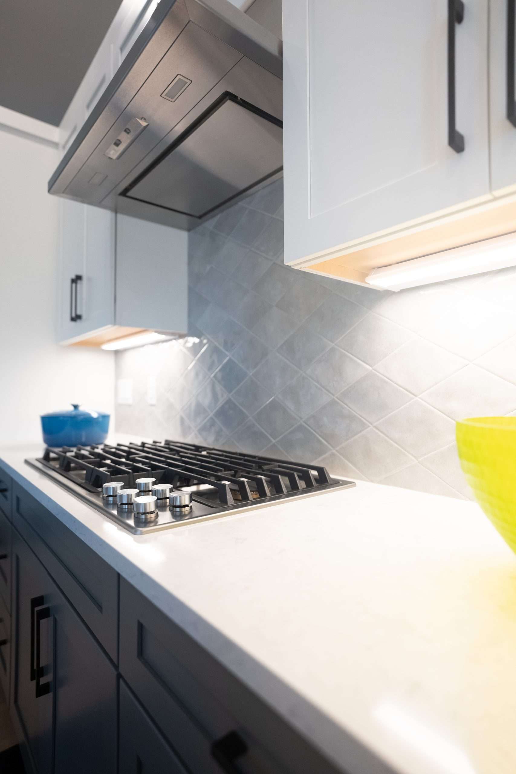 Modern kitchen with gas cooktop, stainless range hood, white countertop, and white cabinets