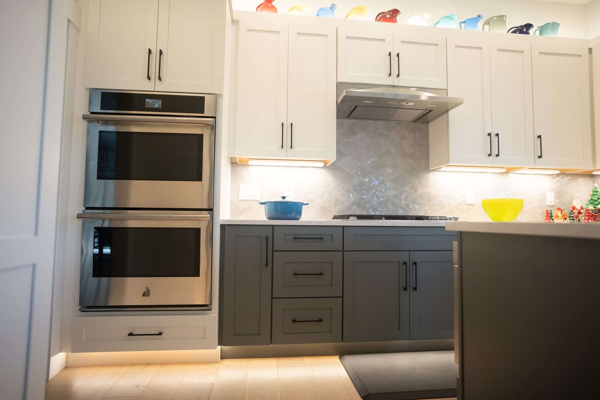 Modern kitchen with white cabinets, built-in stainless oven, gray lower cabinets, and blue and yellow dishes on the counter