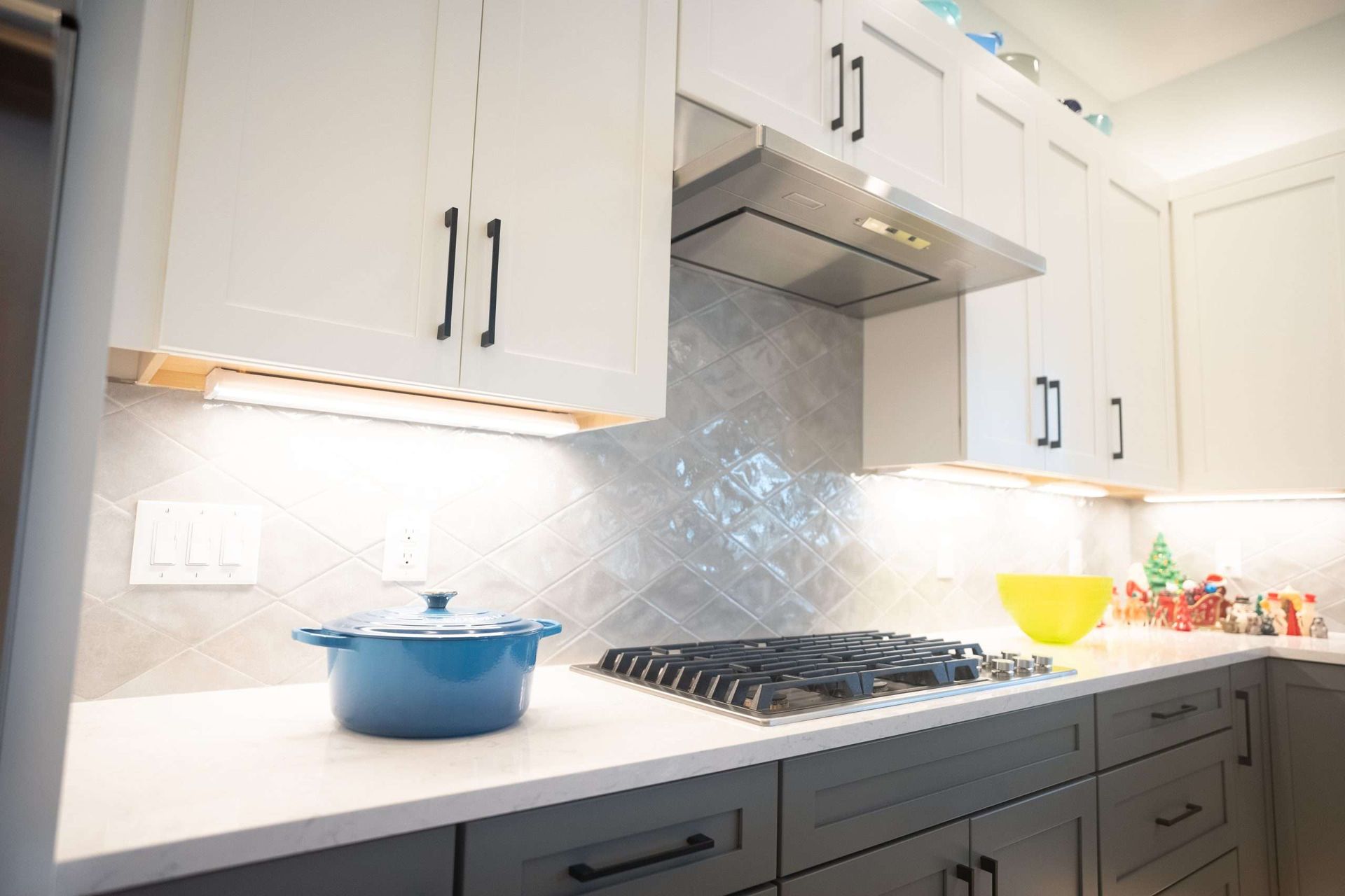 Bright modern kitchen with white cabinets, gray backsplash, gas stove, blue pot, and fruit on the counter