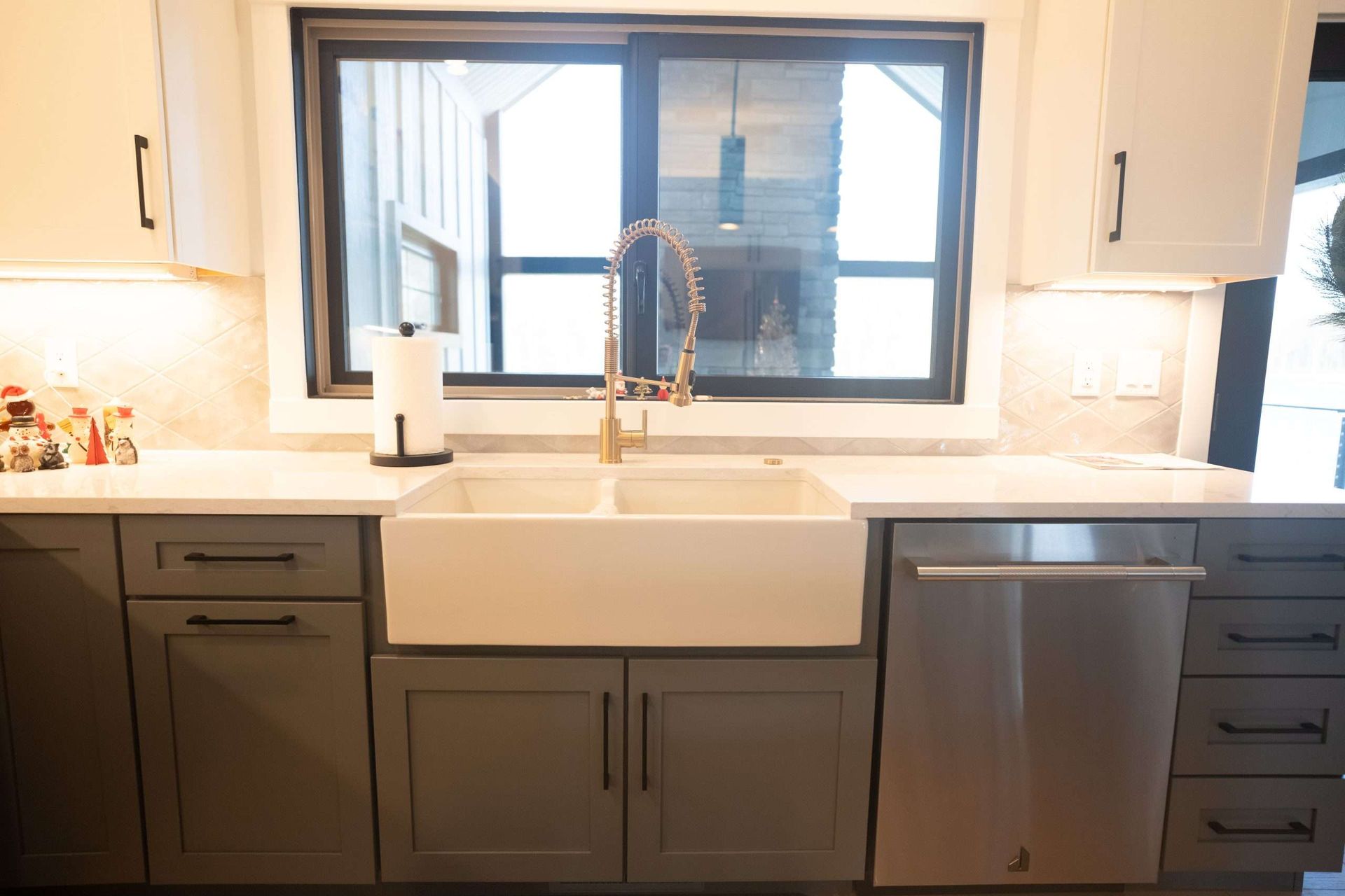 Modern kitchen sink with white apron sink, dark cabinets, stainless dishwasher, and a large window above the counter