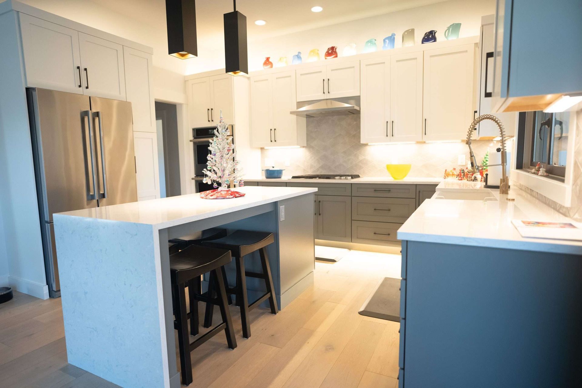 Bright modern kitchen with white cabinets, gray island, stainless fridge, and pendant lights