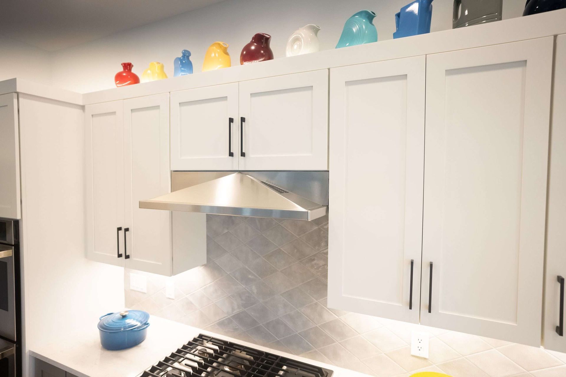 White kitchen cabinets with colorful glass jars on top and a stainless steel range hood above a stove