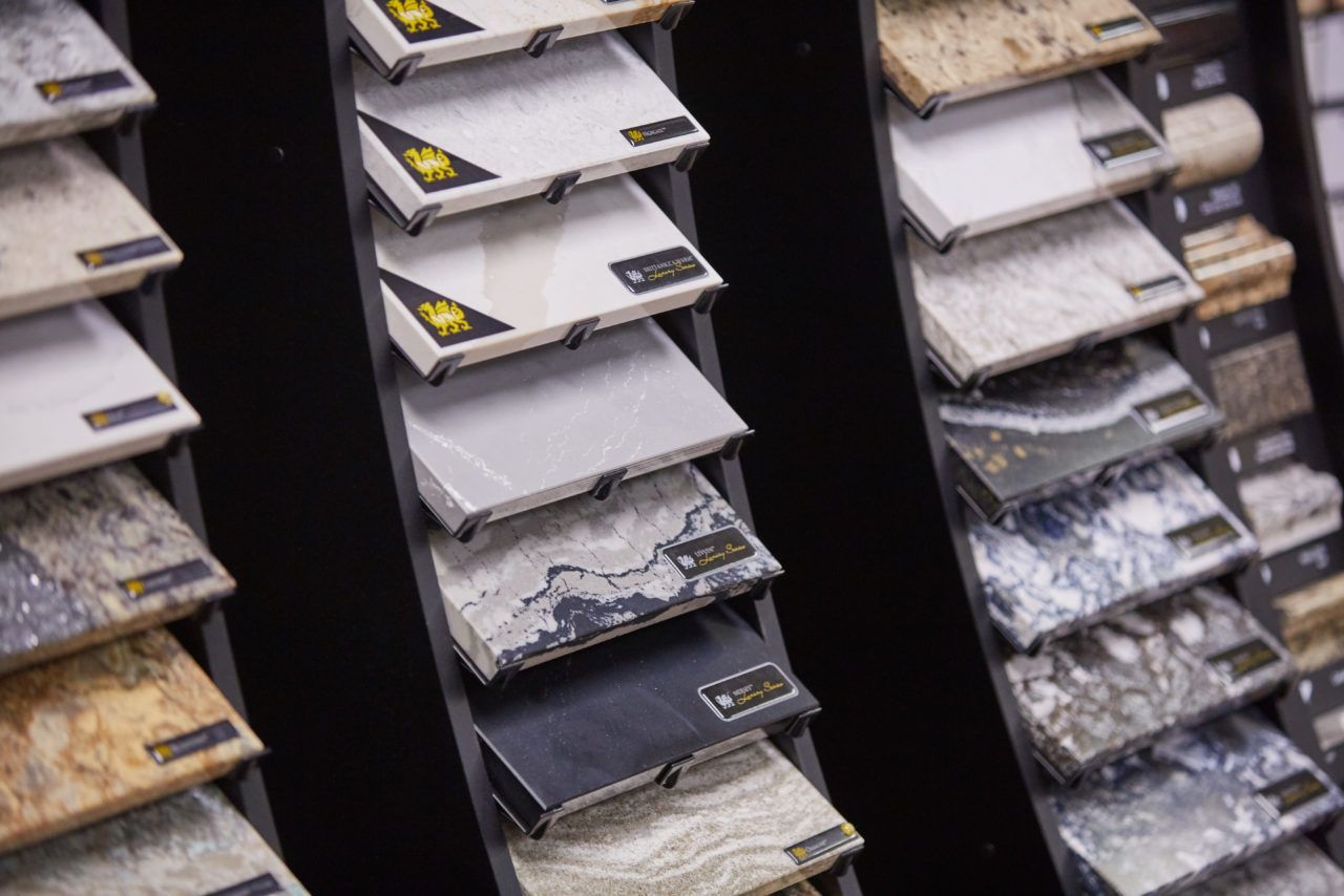 Rows of stone or tile samples in a showroom display, showing various gray and beige finishes.