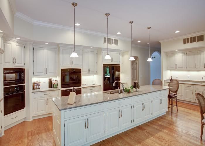 Bright white kitchen with a large island, pendant lights, stainless appliances, and hardwood floors