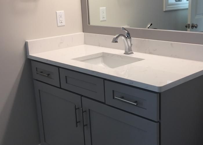 Gray bathroom vanity with white countertop and sink under a wall mirror
