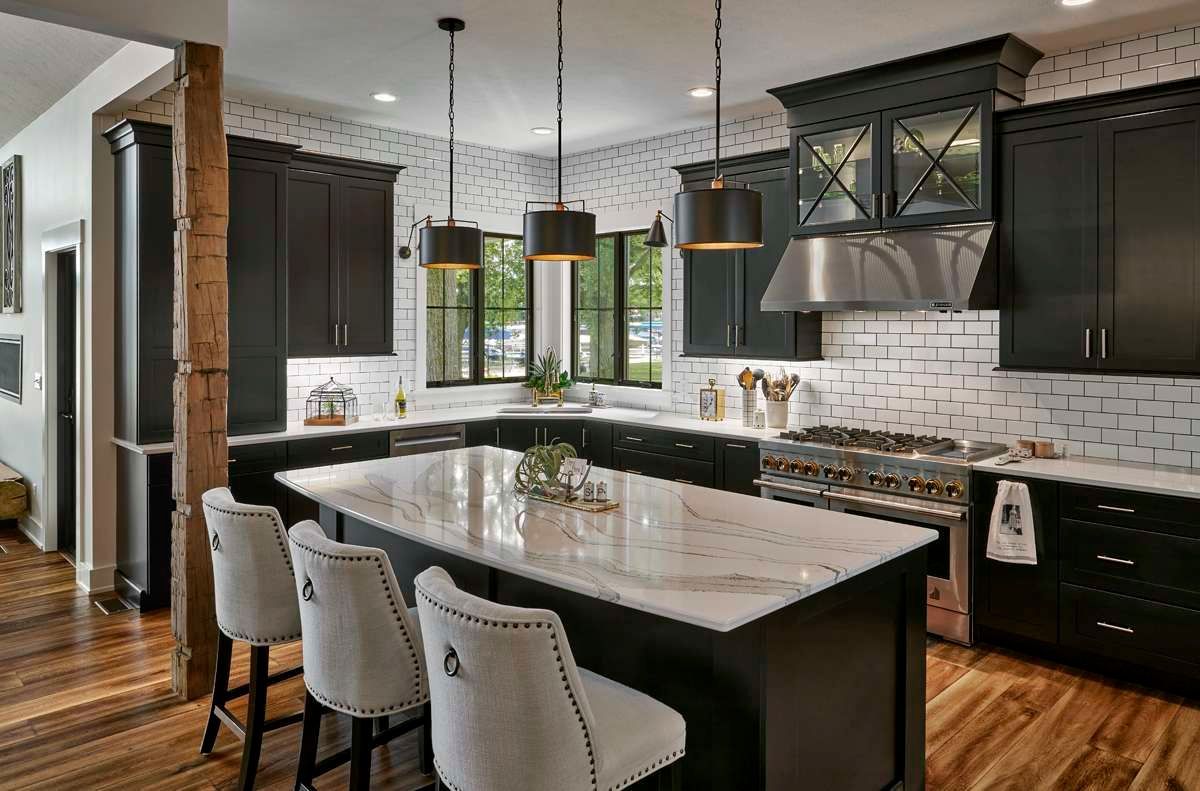 Modern kitchen with dark cabinets, white subway tile, large island, pendant lights, and hardwood floors