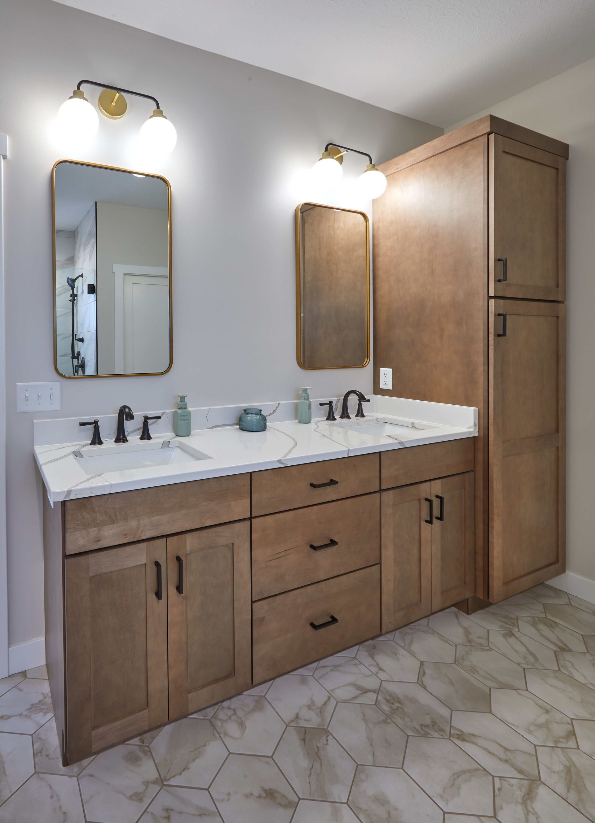 Bathroom vanity with double sinks, wood cabinets, mirrors, and wall sconces on a tiled floor