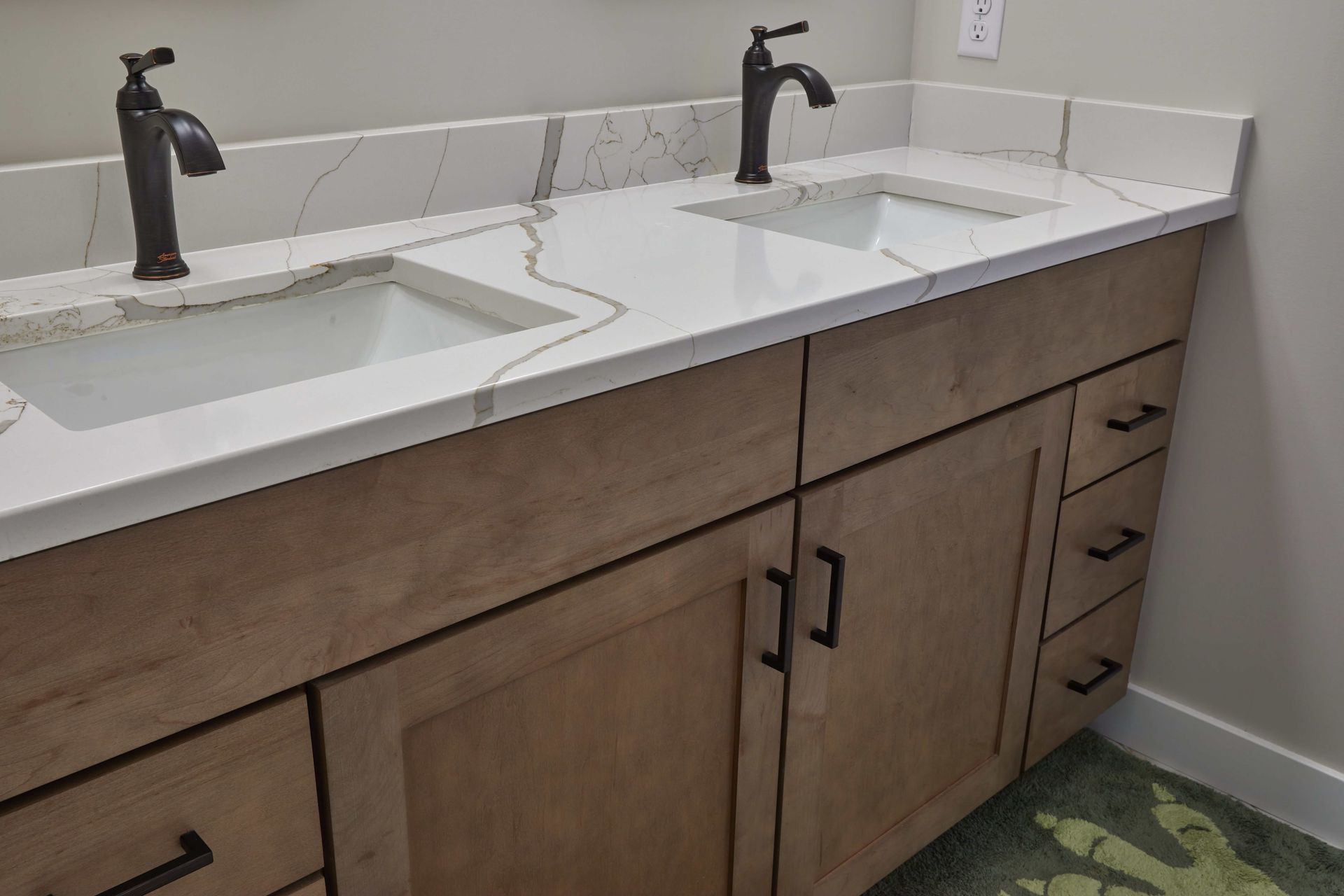 Double vanity with two white sinks, dark faucets, and wood cabinets in a bathroom.