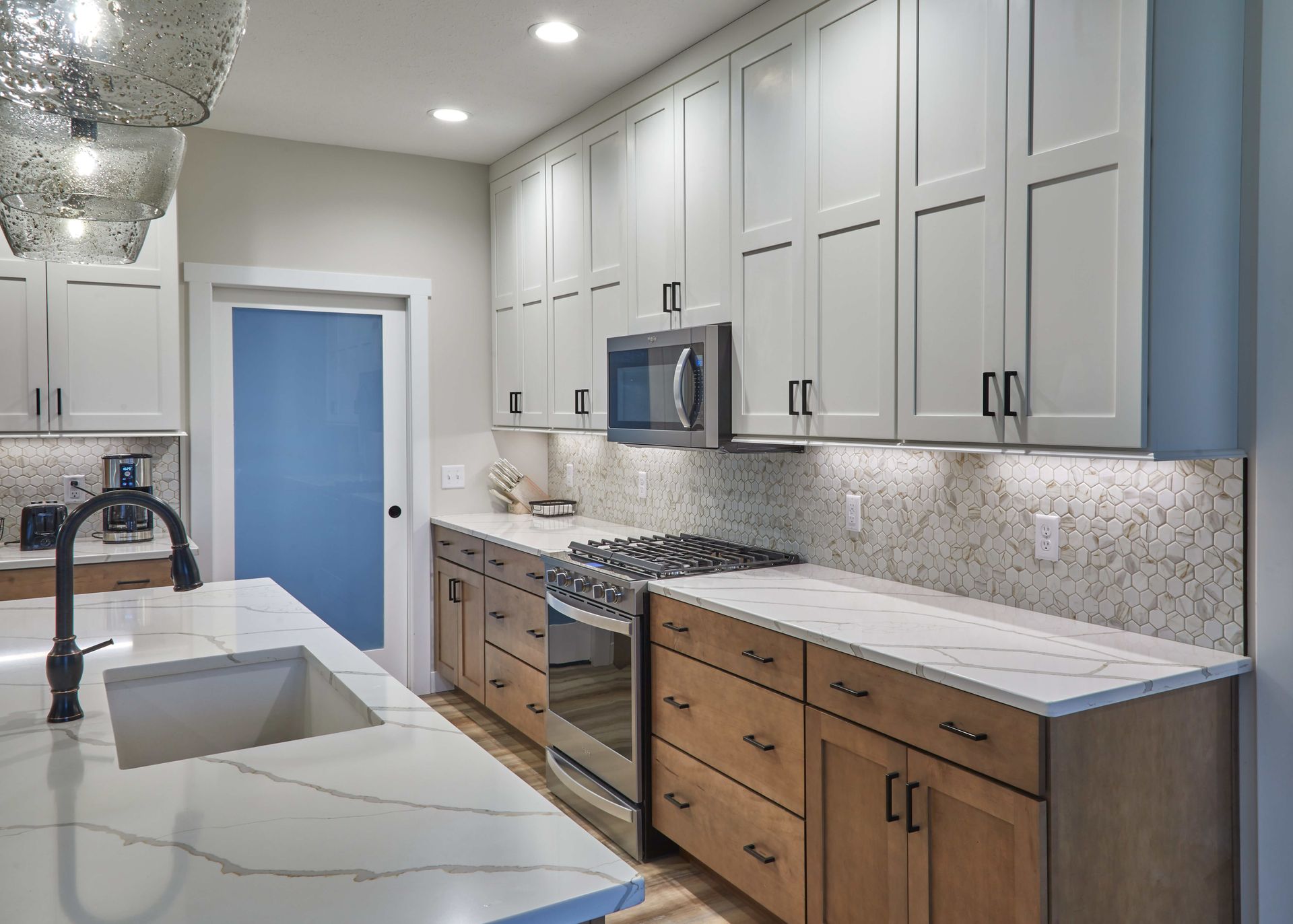 Modern kitchen with white cabinets, marble island, wood lower cabinets, and stainless steel appliances