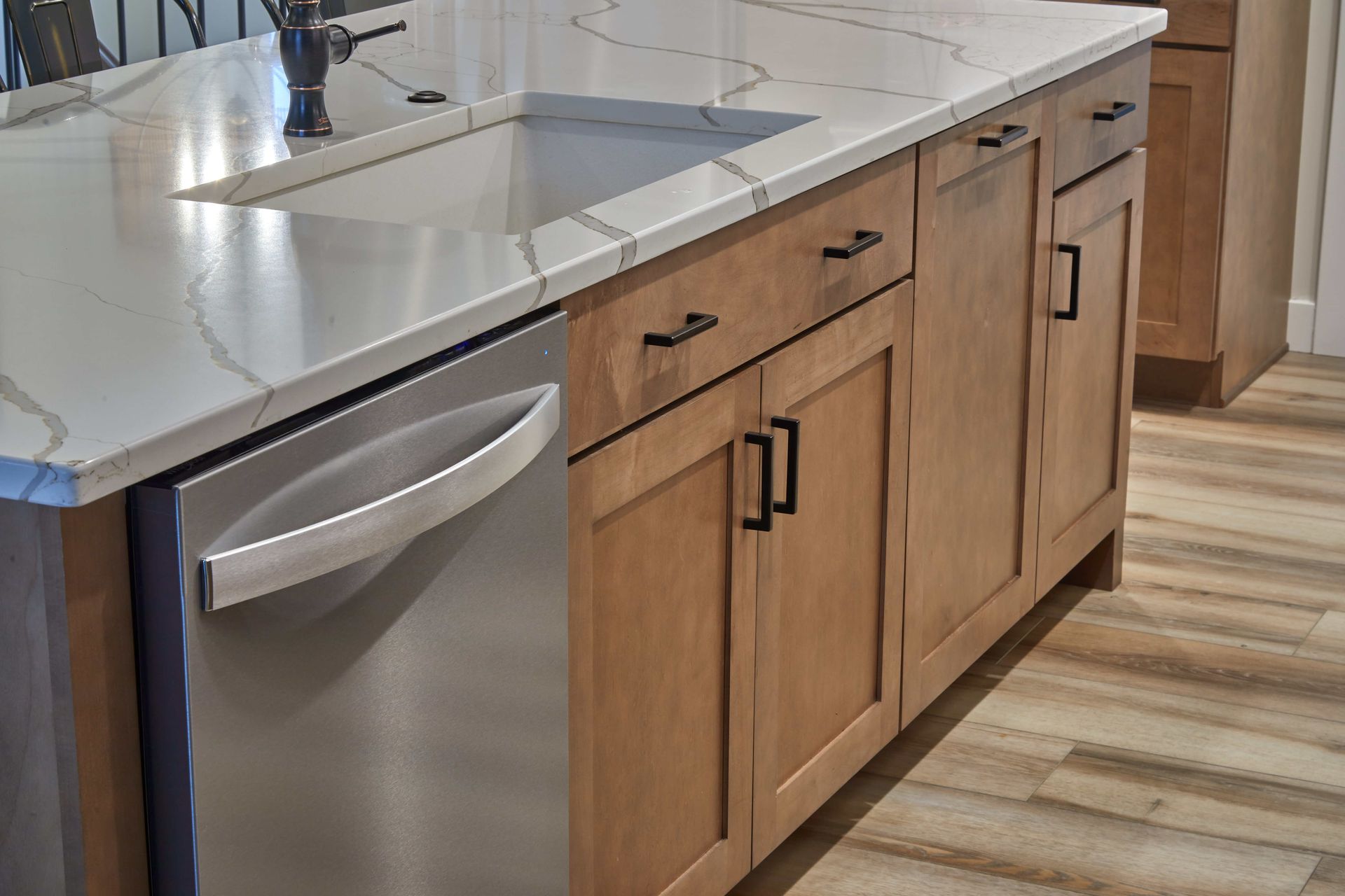 Kitchen sink with white countertop, stainless dishwasher, and light wood cabinets with black handles