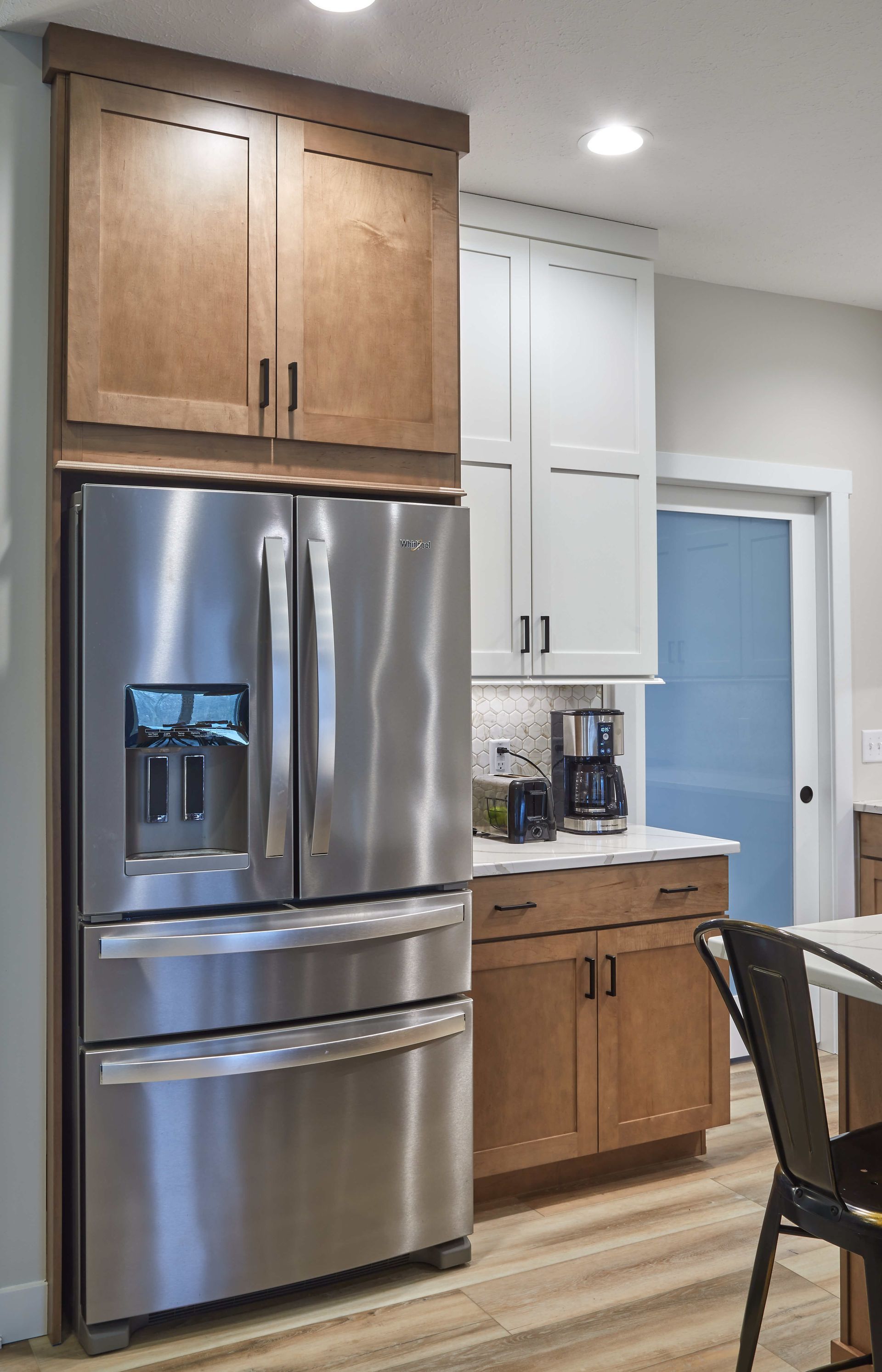 Kitchen with stainless steel refrigerator, wooden cabinets, white upper cabinets, and a coffee maker on the counter