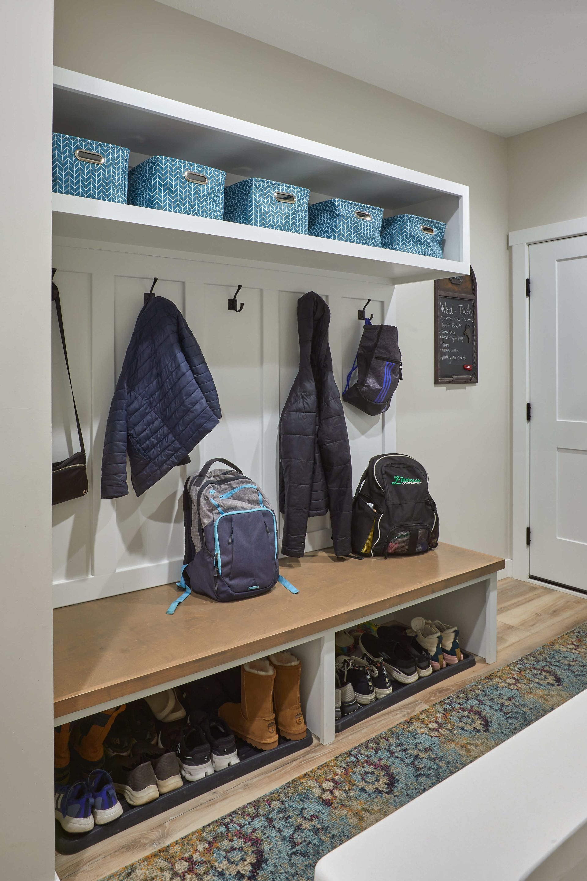 Mudroom bench with shoes and backpacks, coat hooks, white walls, and a window above the storage area