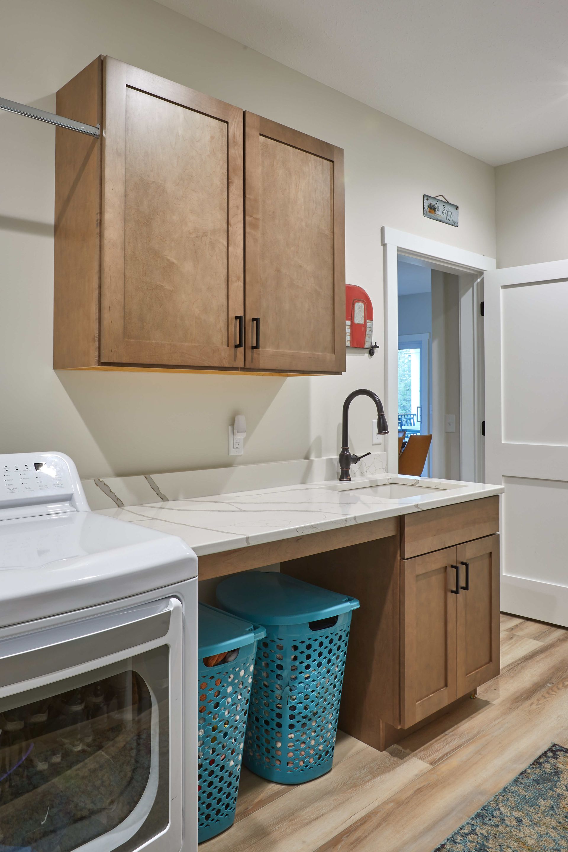 Laundry room with washer, sink, wooden cabinets, and blue baskets on a countertop