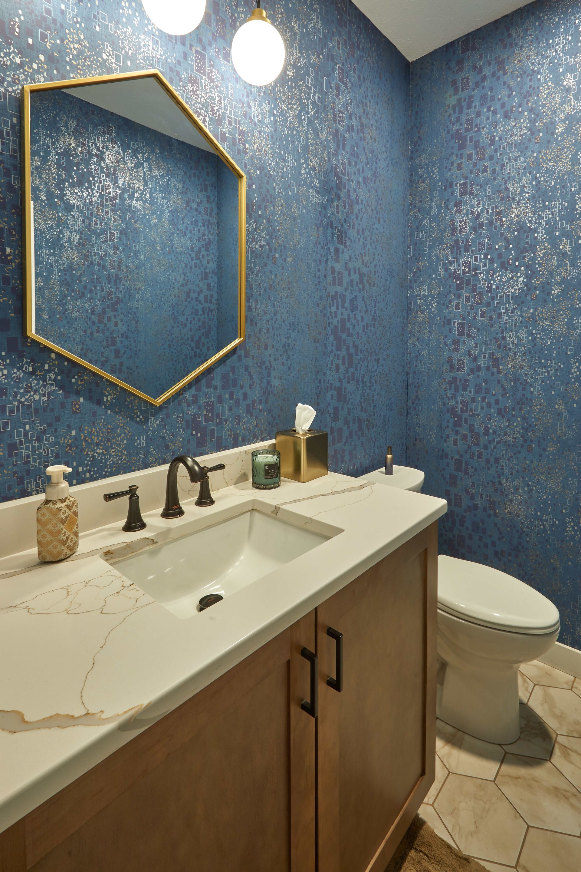 Small bathroom with blue textured walls, gold hexagon mirror, white vanity, and toilet.