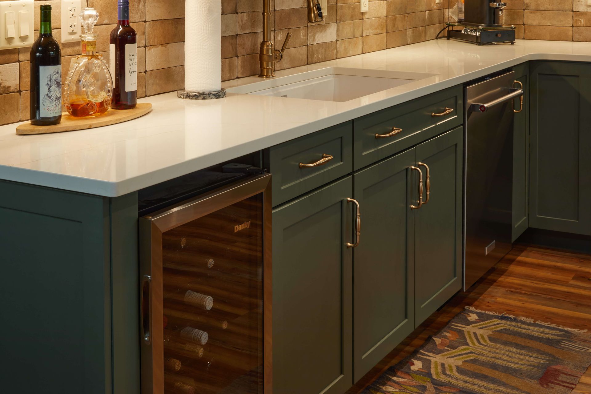 Modern kitchen with dark green cabinets, white countertop, and a built-in wine cooler under the counter