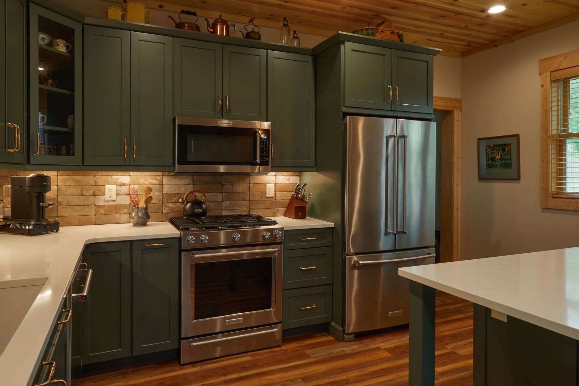 Modern kitchen with dark green cabinets, stainless appliances, wood ceiling, and a white island