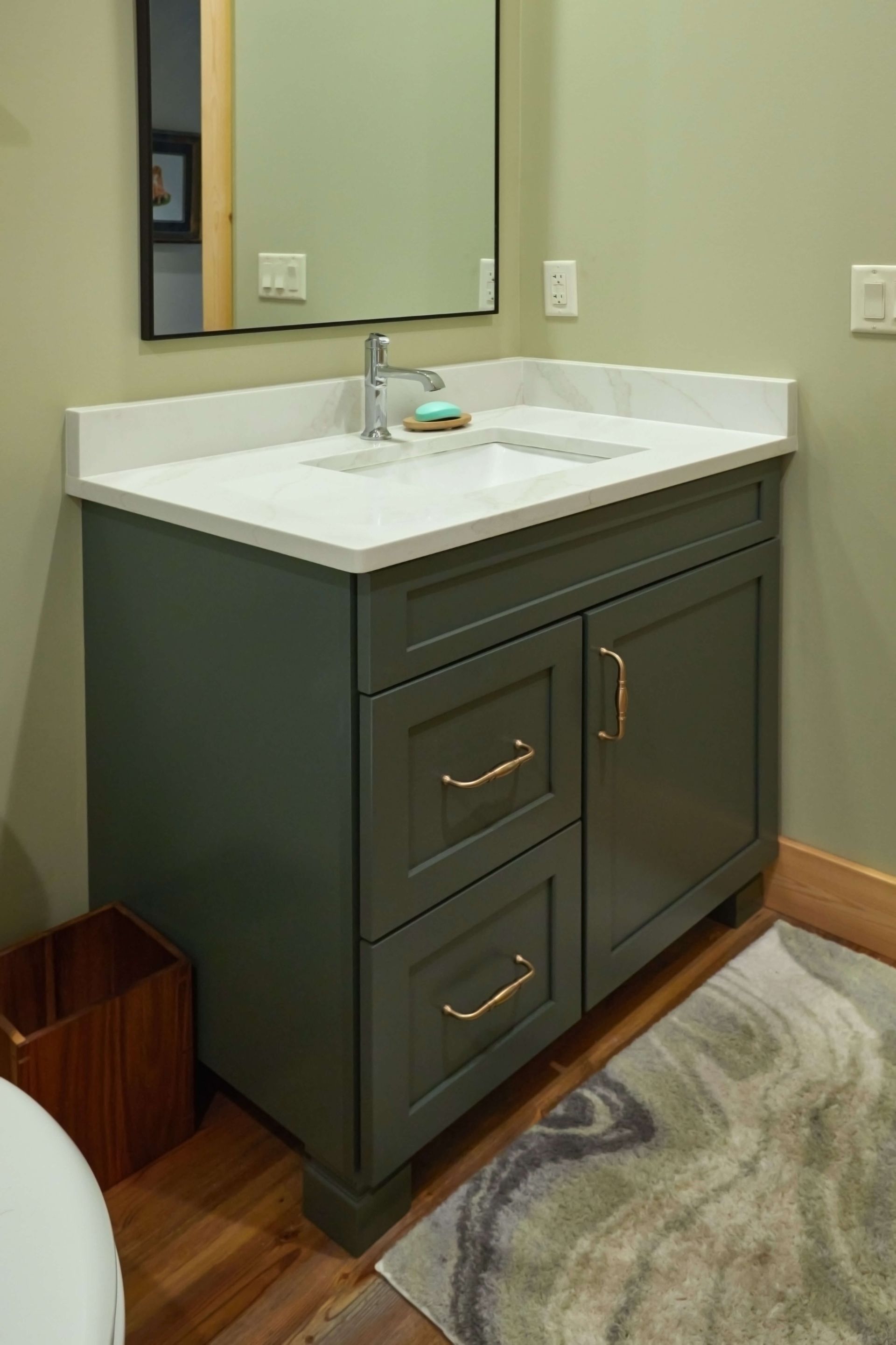 Dark green bathroom vanity with white sink and mirror in a small bathroom