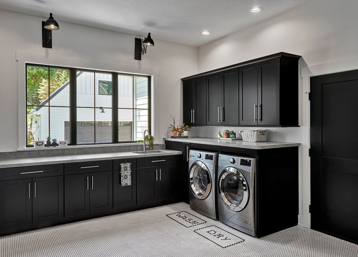 Modern black-and-white laundry room with washer and dryer, cabinets, sink, and large window.