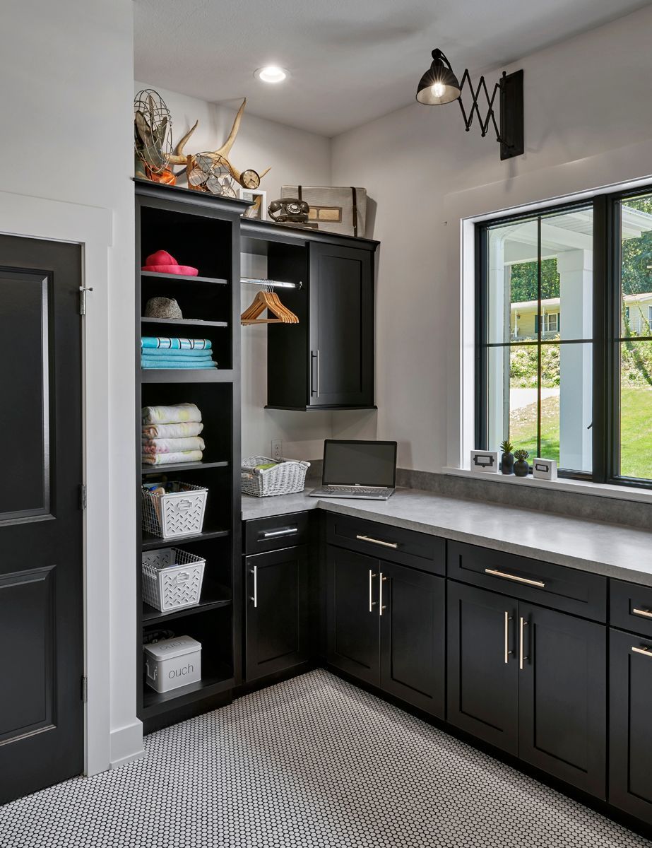 Modern laundry room with black cabinets, white countertop, shelving, and a window overlooking greenery