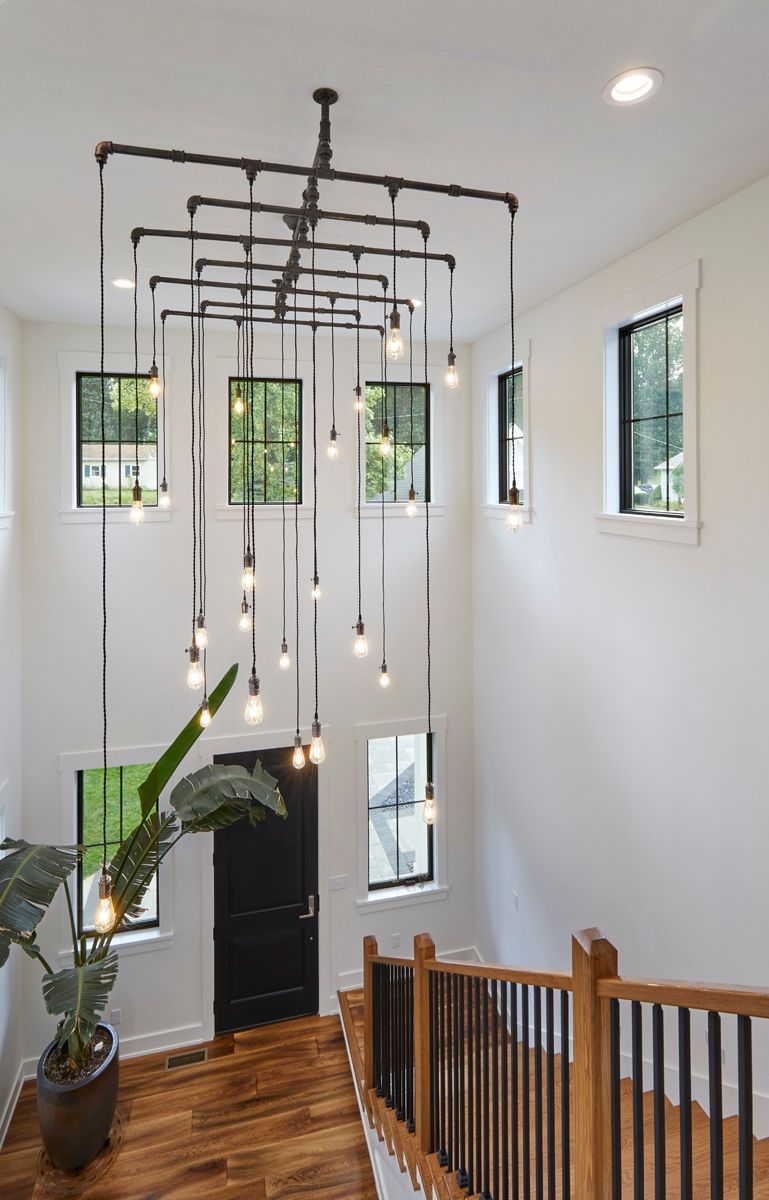 Stairwell with hanging pendant lights, white walls, wood railing, and small windows above the stairs
