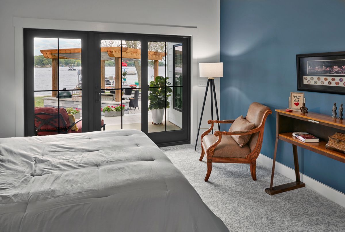 Modern bedroom with bed, blue accent wall, wicker chair, desk, and sliding glass doors to a patio