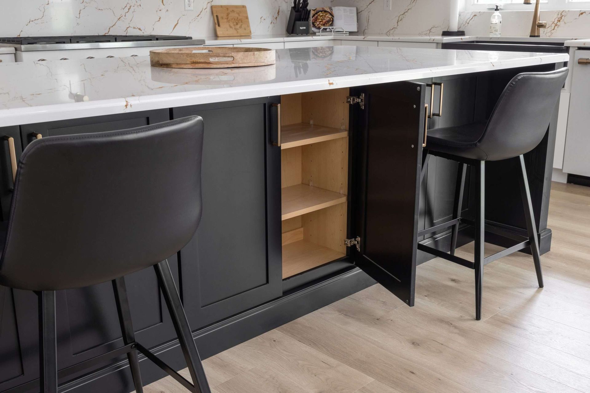 Kitchen island with two black bar stools and open cabinet shelves below a white countertop