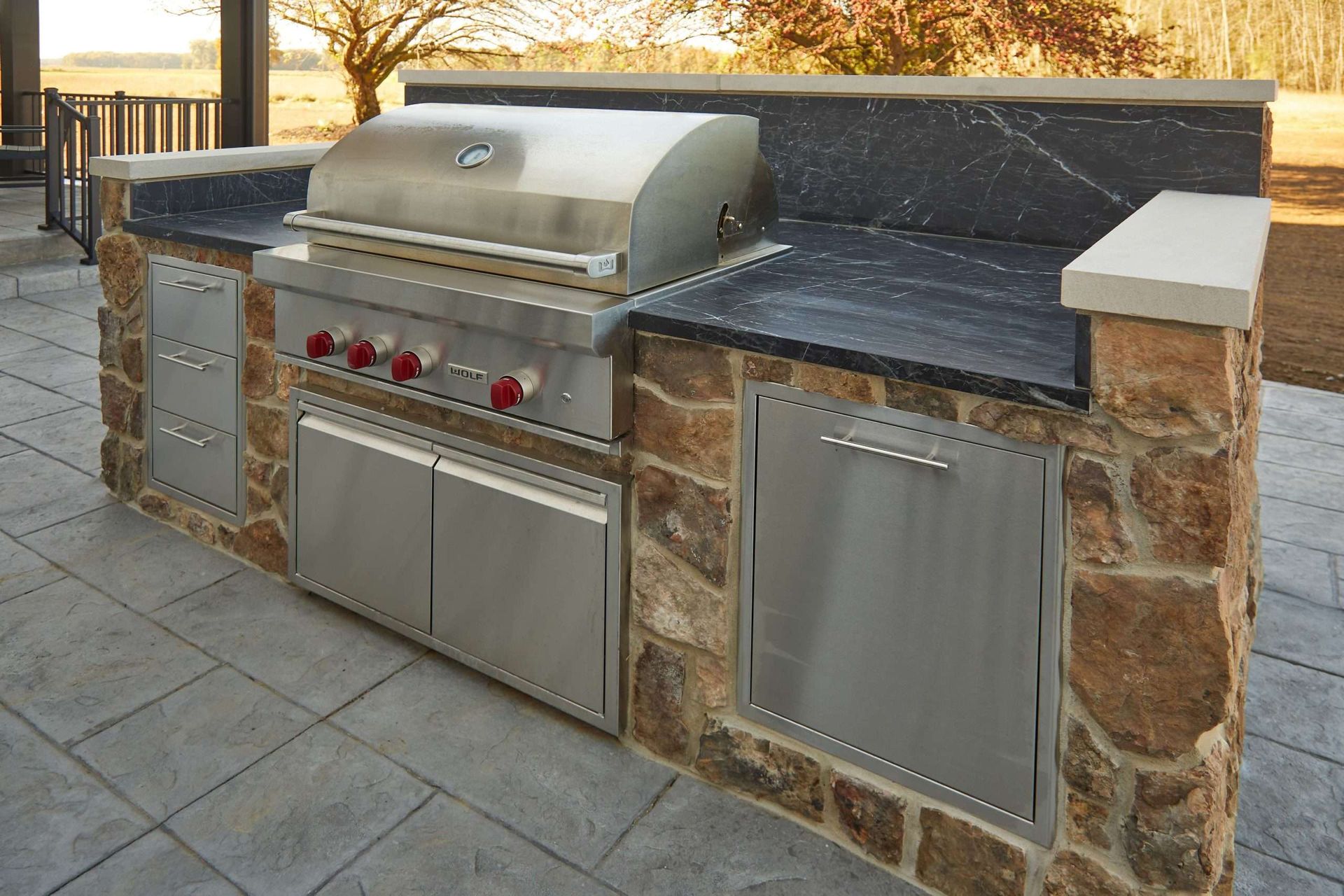 Outdoor stone barbecue grill with stainless steel doors and black countertop on a patio