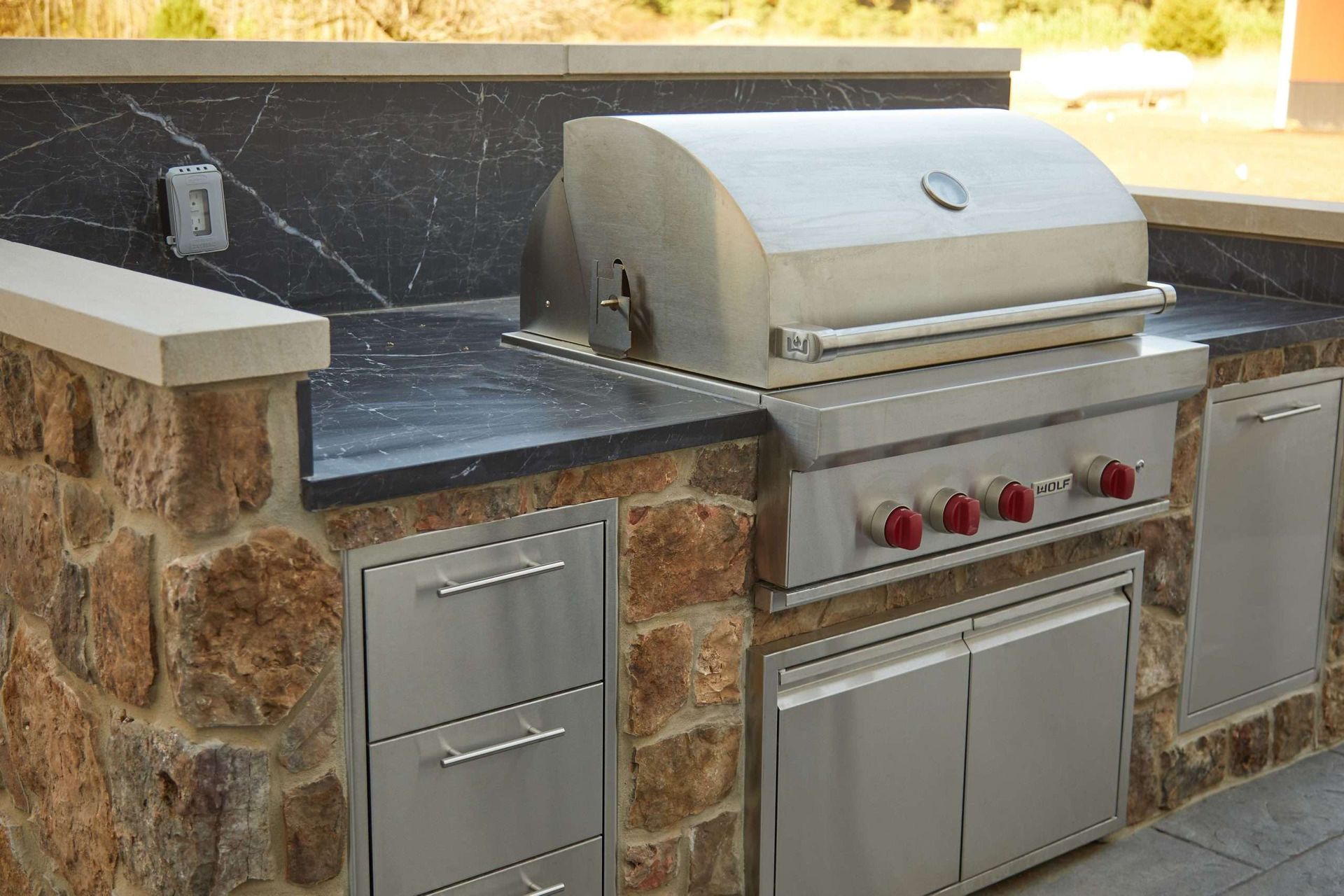 Outdoor built-in stainless steel grill with stone countertop and red control knobs