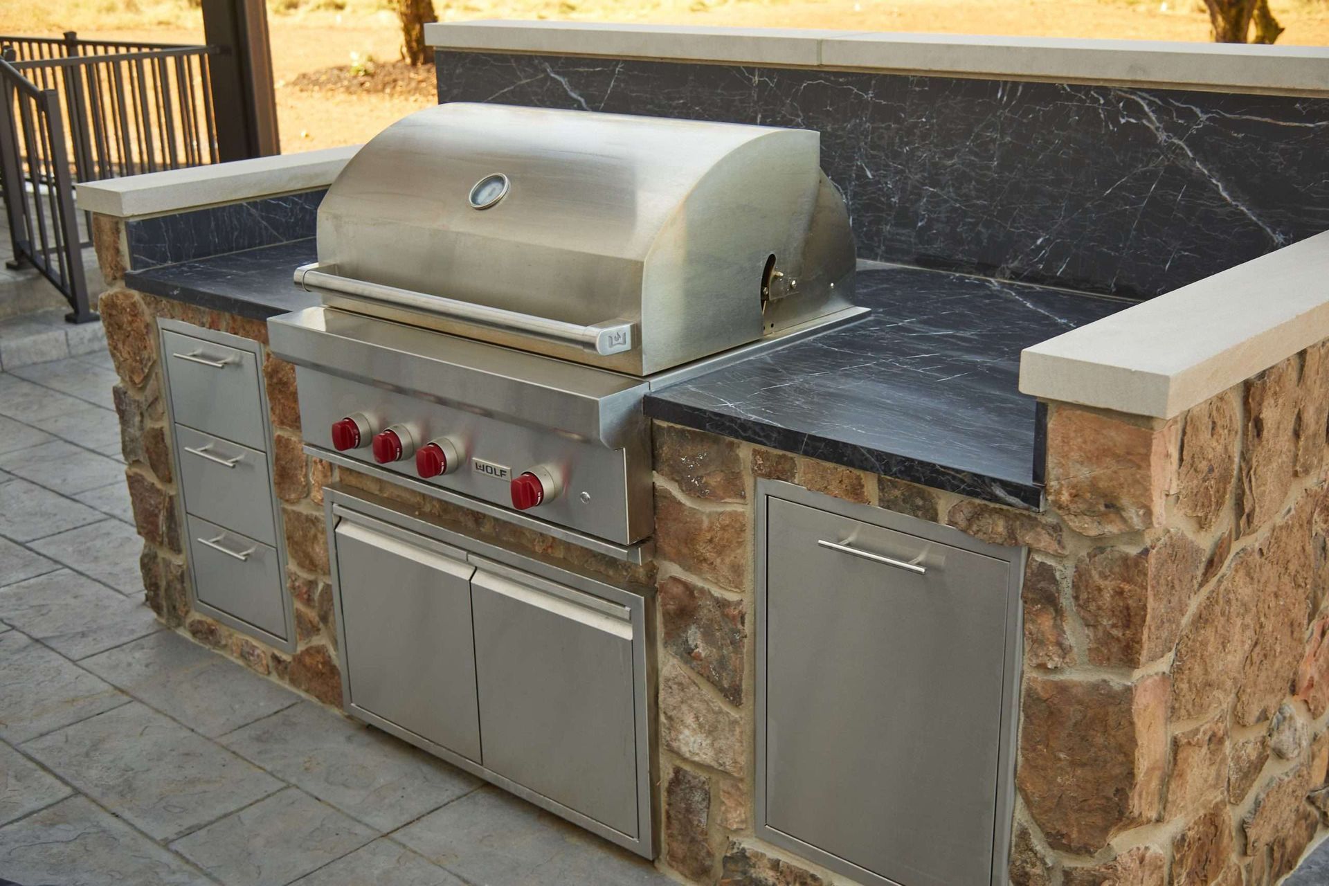 Outdoor stainless steel grill island with stone counters and cabinets built into a patio wall