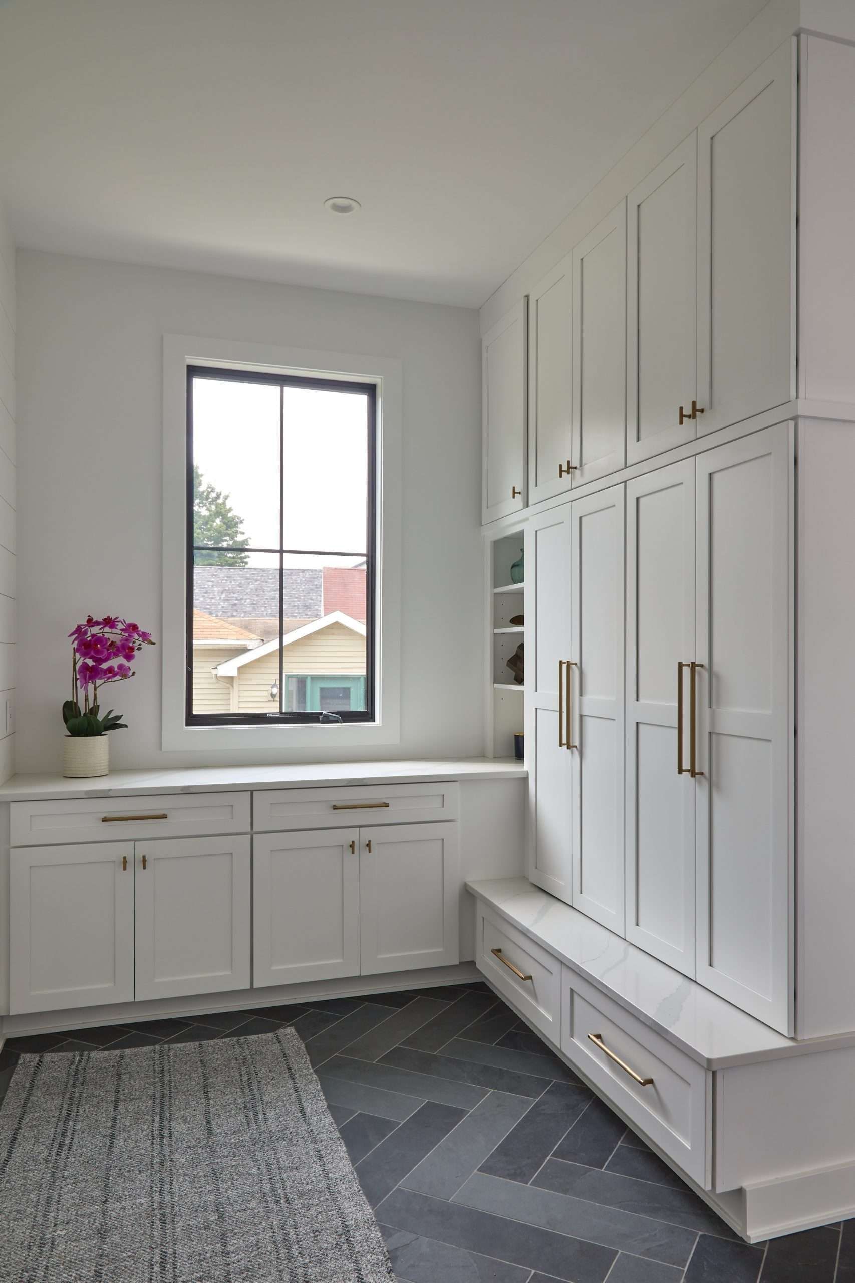 Bright laundry room with white cabinets, built-in storage, window, and gray patterned rug