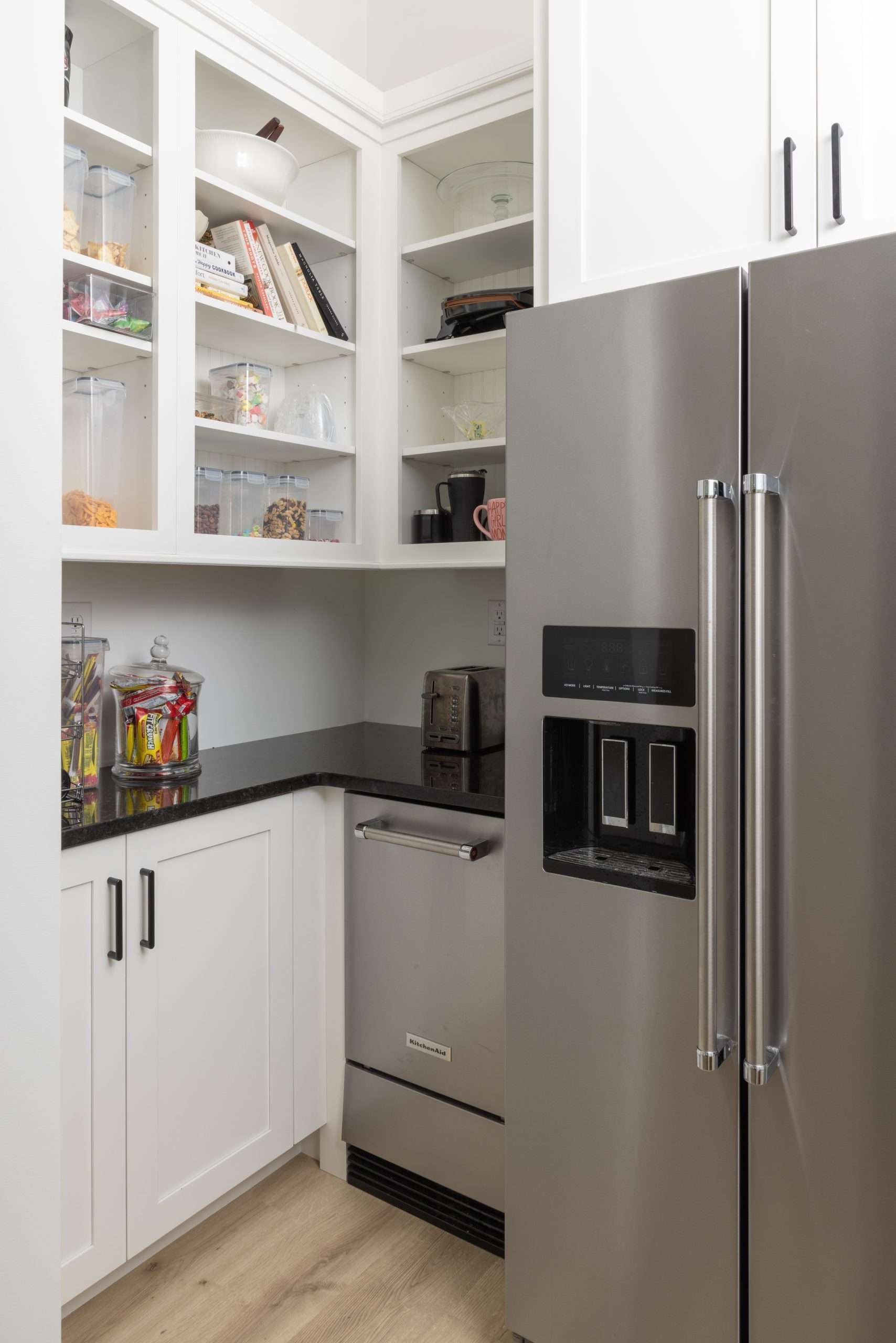 Modern kitchen corner with white cabinets, open shelves, gray countertop, and stainless steel fridge.