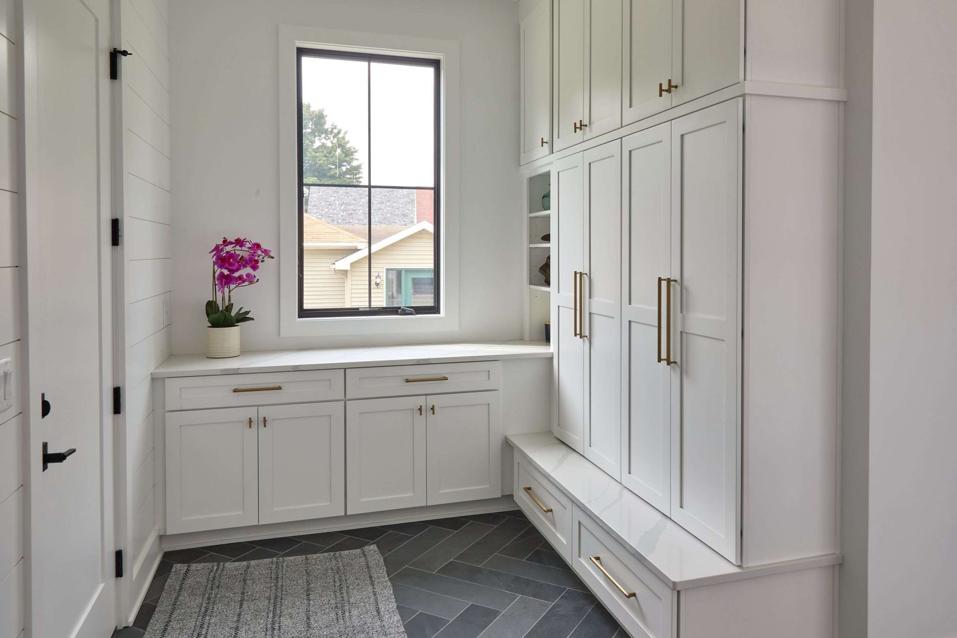 Bright white mudroom with built-in cabinets, bench, window, and a potted orchid
