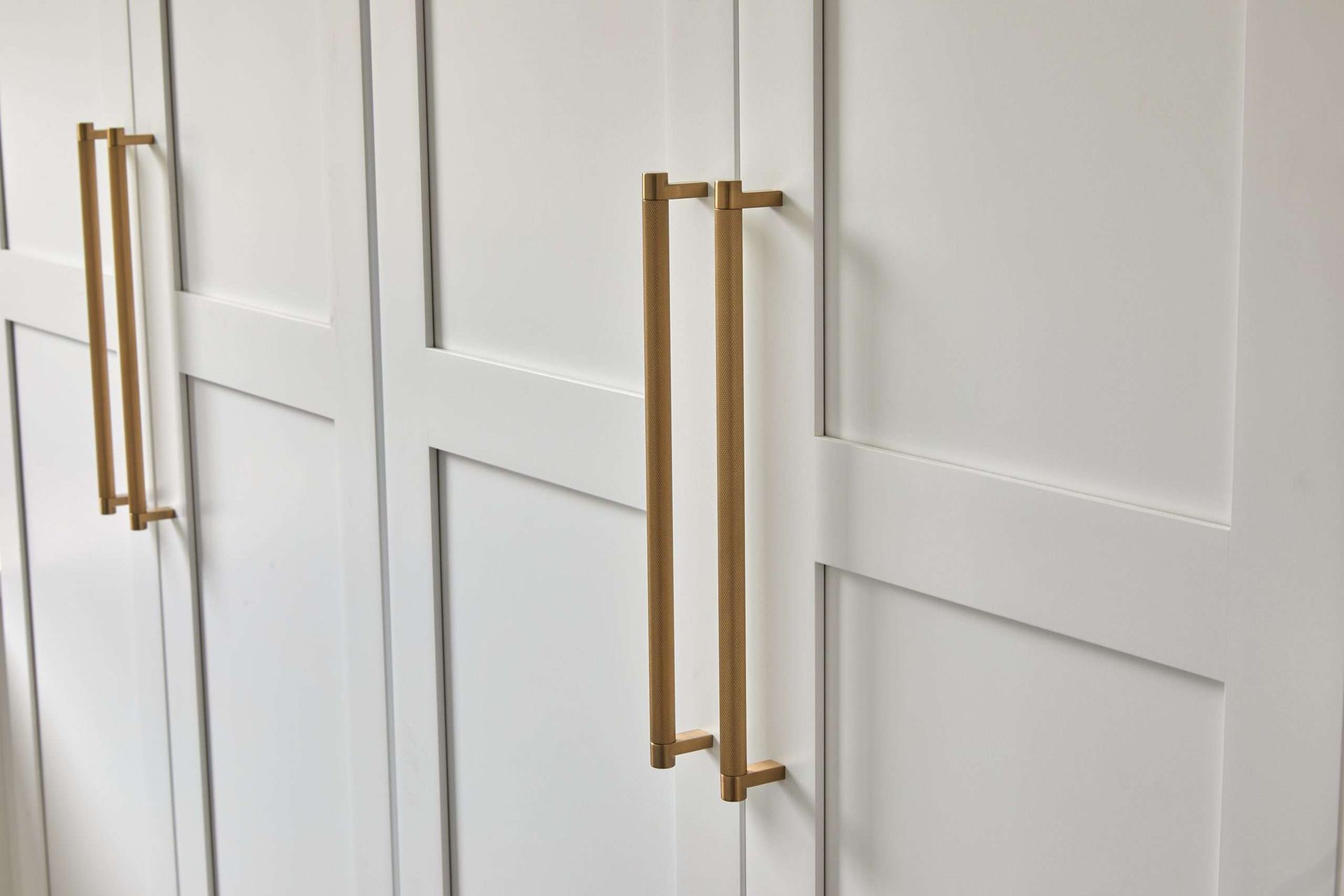 White cabinet doors with long gold handles in a bright room