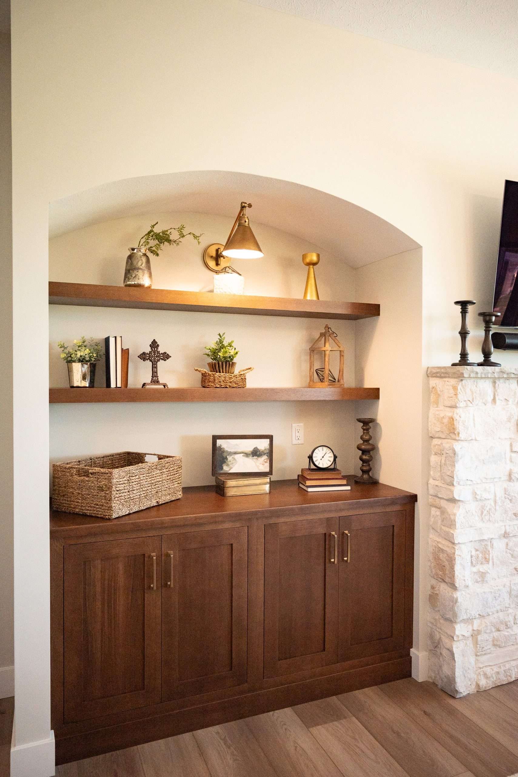 Built-in wall niche with wood cabinet, shelves of decor, and a stone fireplace edge.