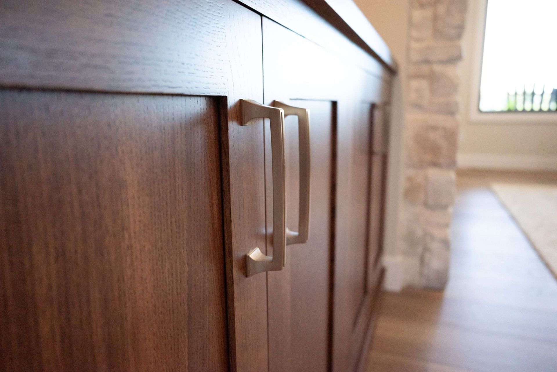 Wooden cabinet with silver handles in a bright hallway near a stone wall and window