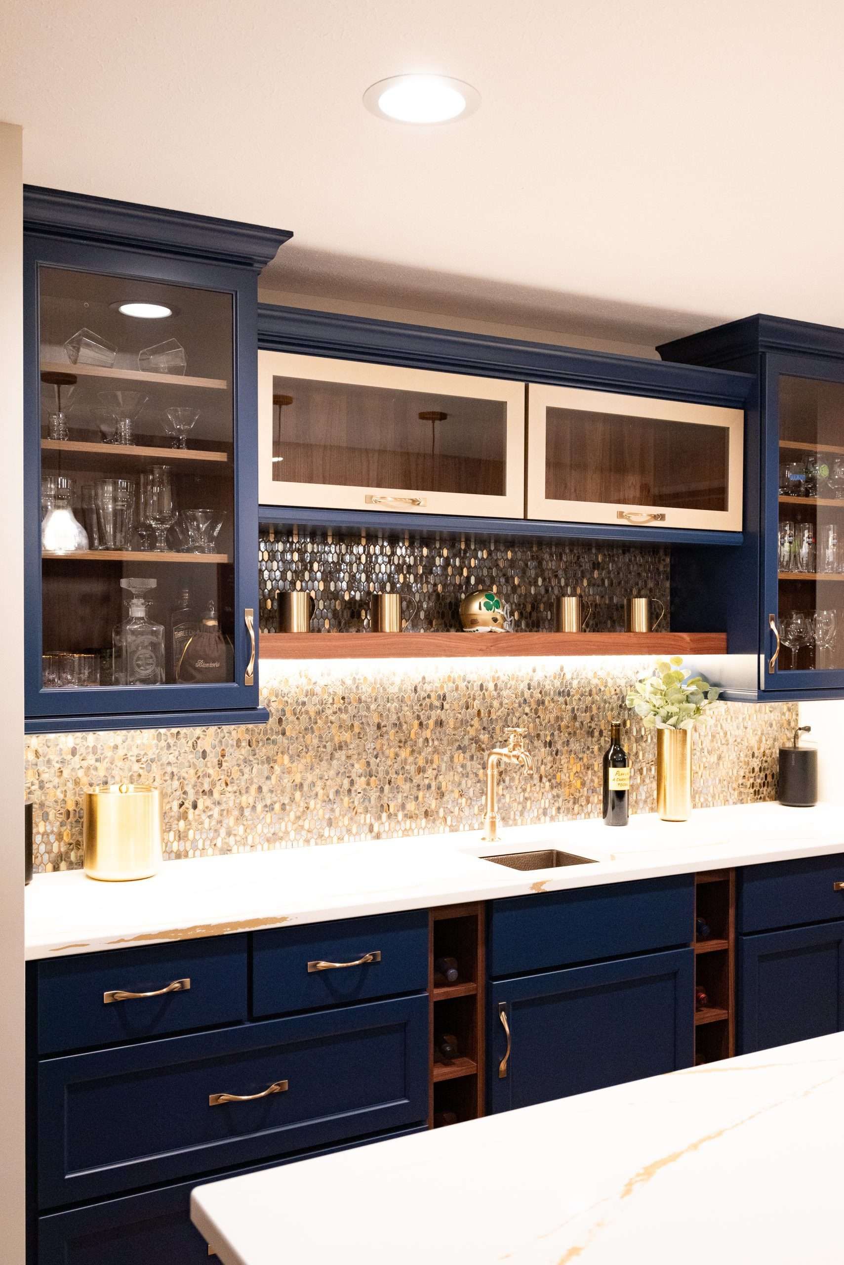 Blue kitchen cabinets with glass-front doors and a white countertop, decorated with warm under-cabinet lighting