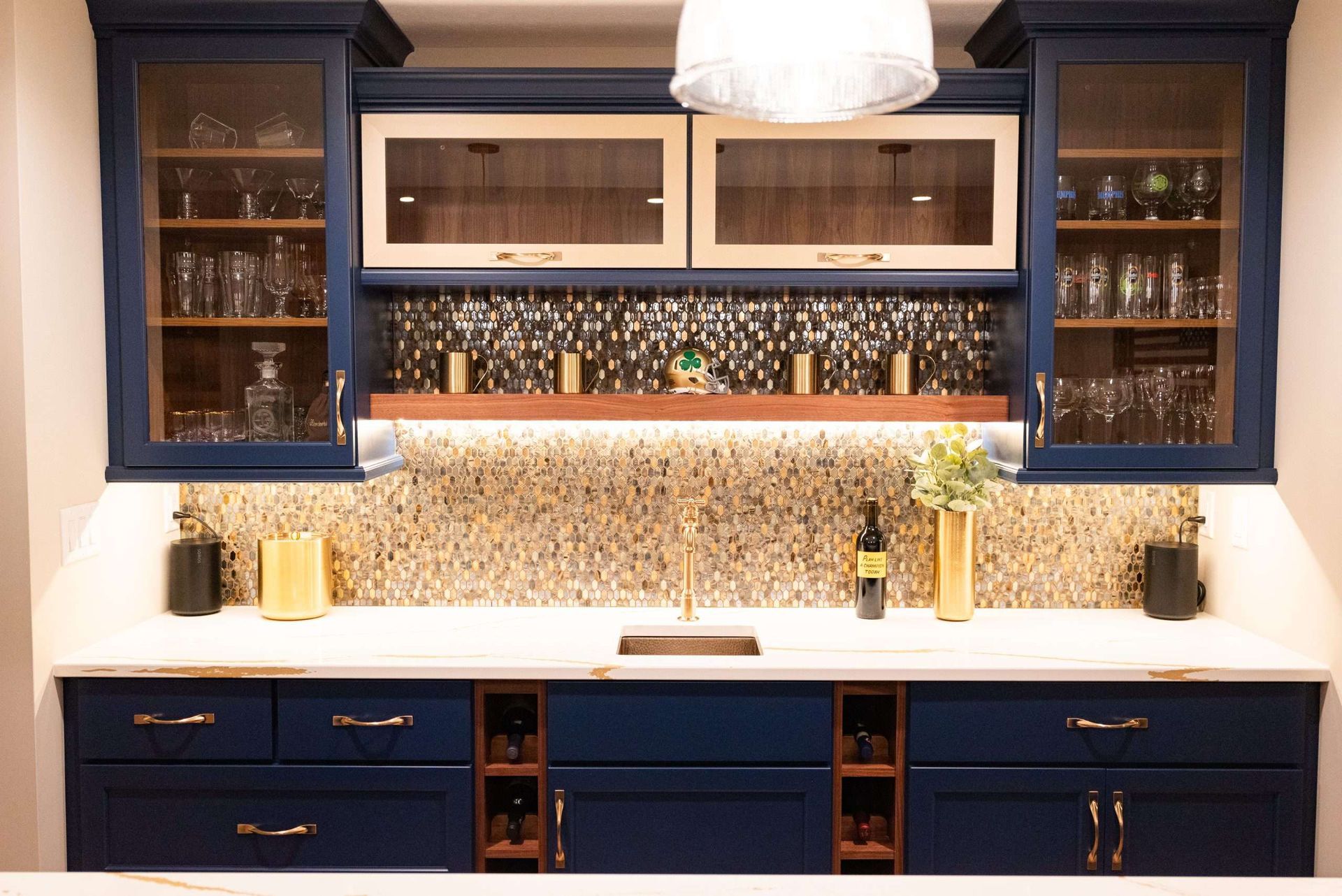 Blue kitchen bar with white countertops, mosaic backsplash, glass cabinets, and shelves of bottles and glasses