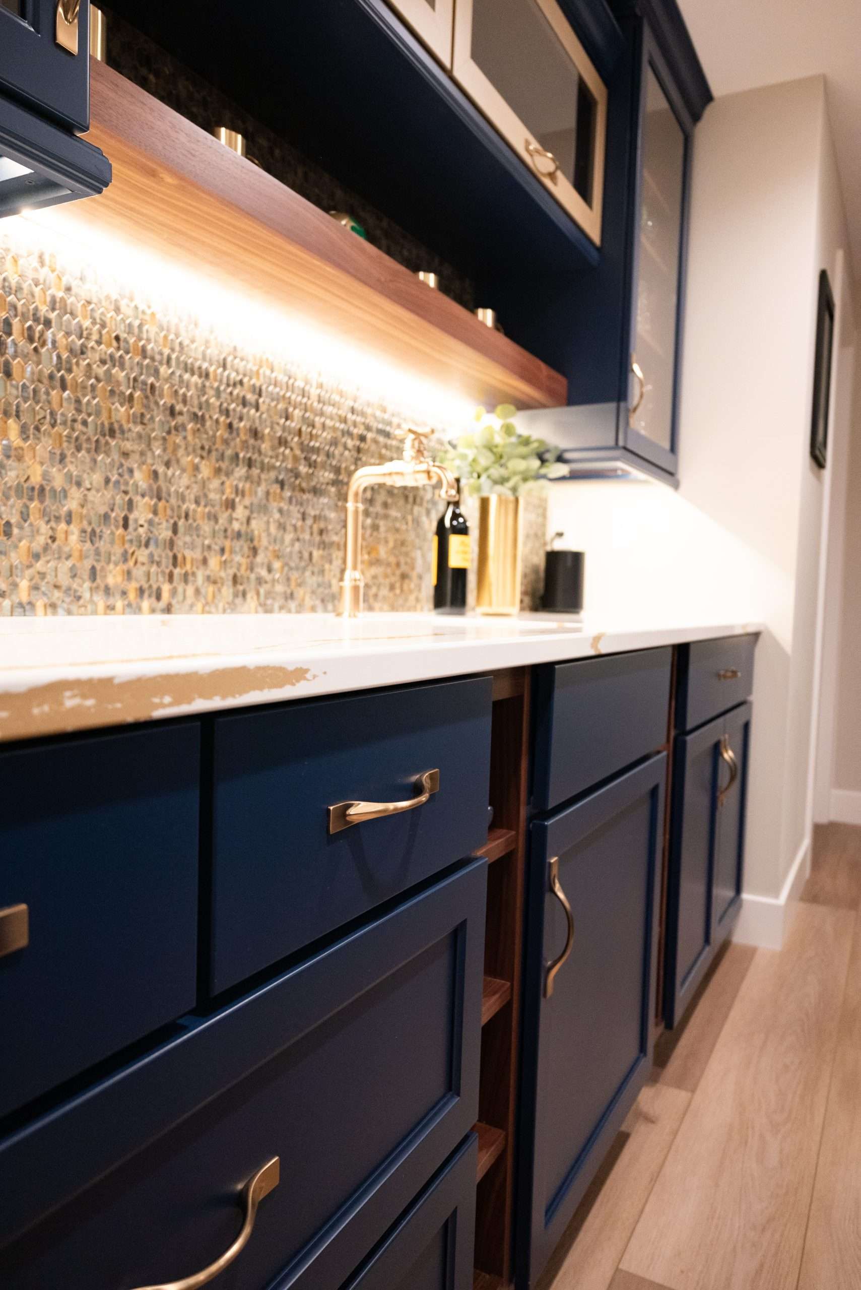 Modern kitchen with navy cabinets, white countertops, and under-cabinet lighting on a tiled backsplash