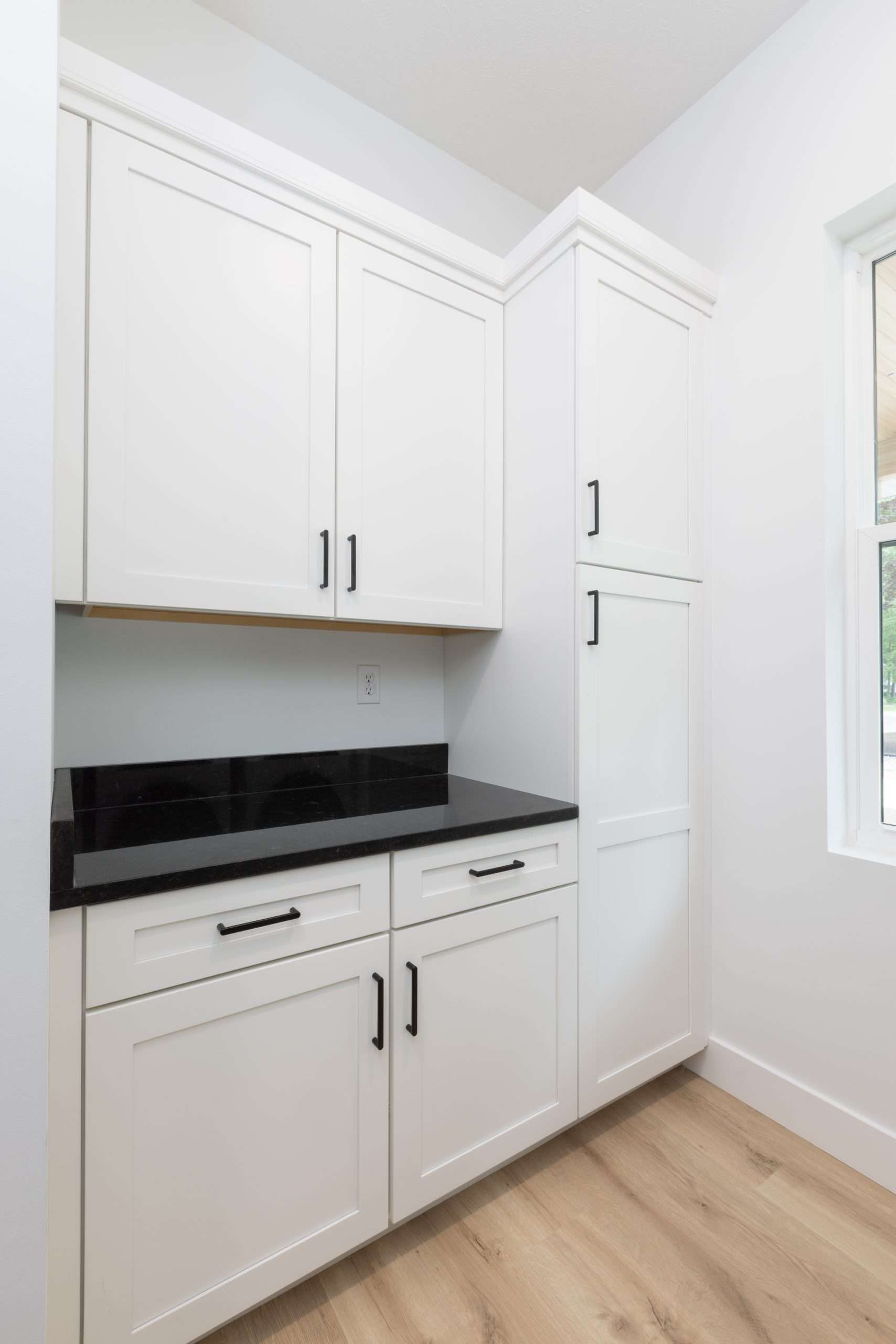 White built-in kitchen cabinets with black countertop and light wood floor in a bright corner room