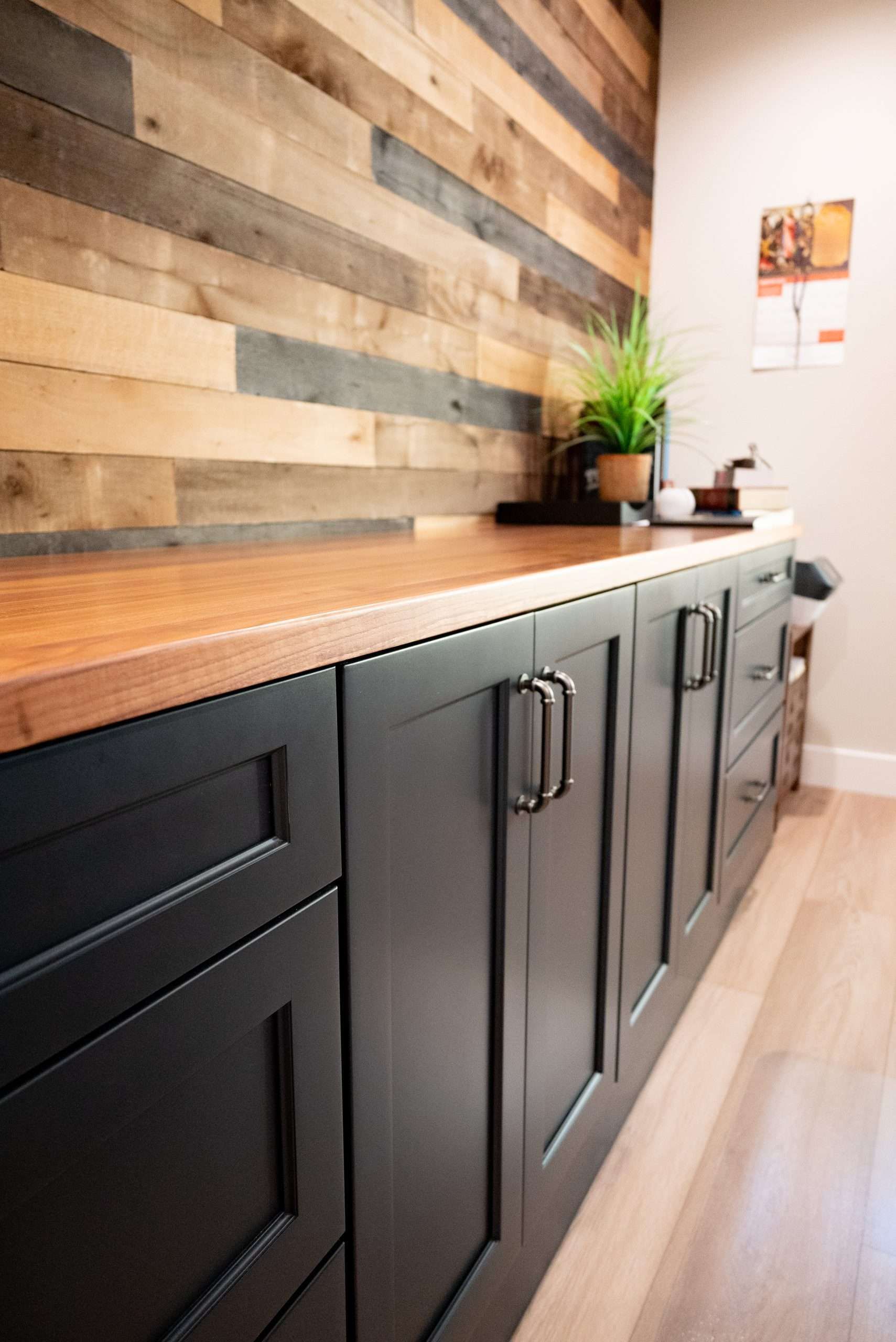Dark kitchen cabinets with wood countertop and rustic wood accent wall in a bright room