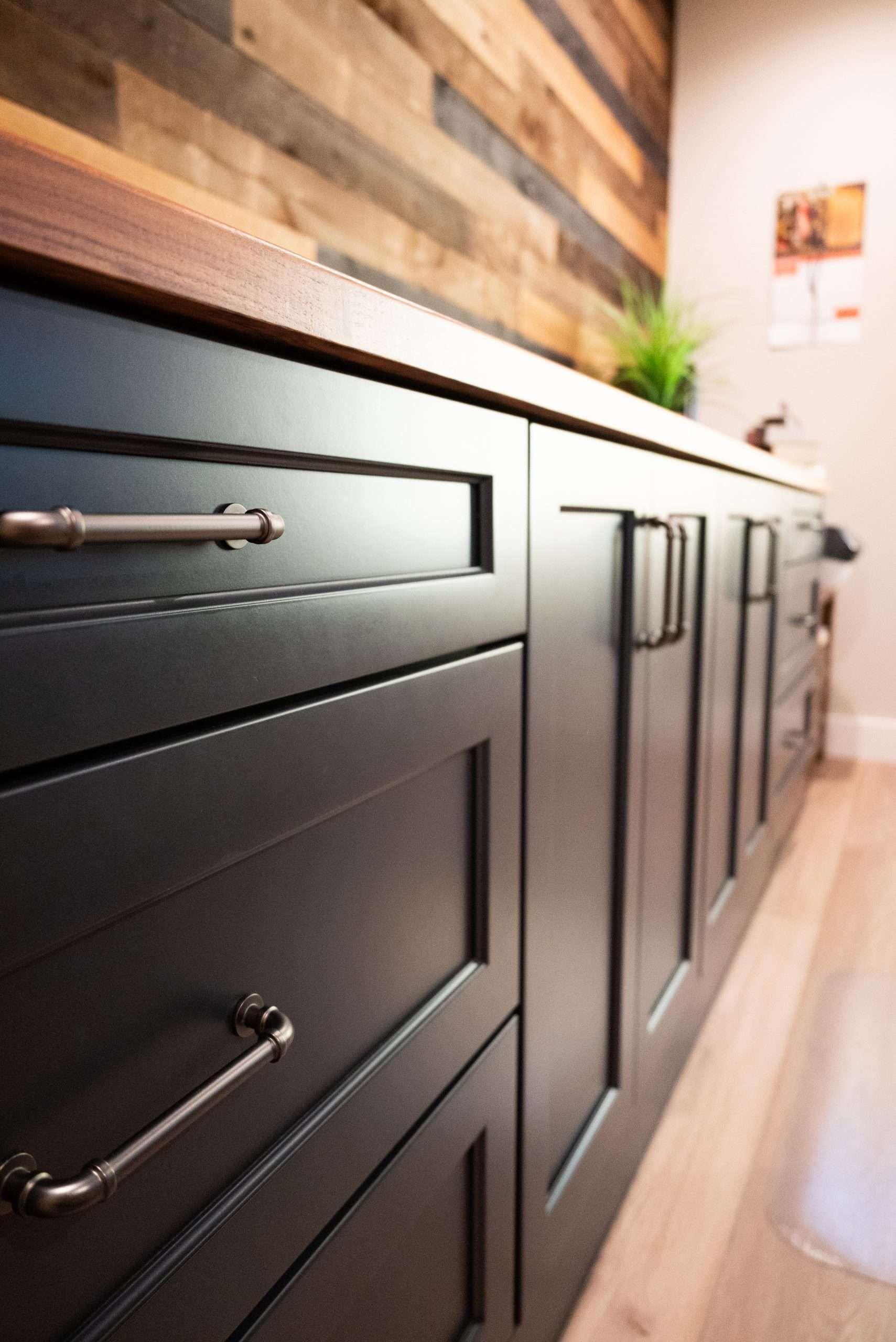 Dark kitchen cabinets with silver handles along a wooden countertop and backsplash, viewed at an angle.