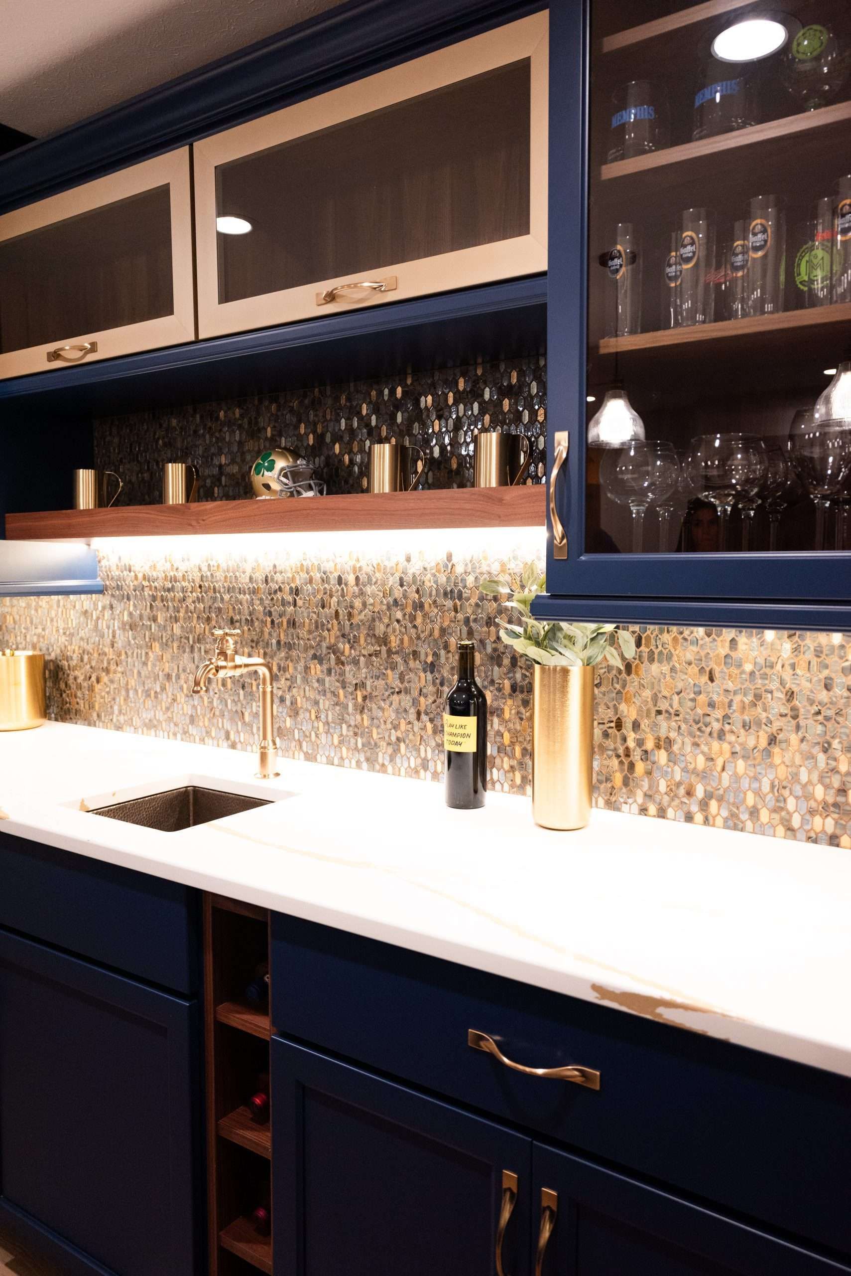 Modern kitchen with dark blue cabinets, white countertop, mosaic backsplash, and sink under warm lighting