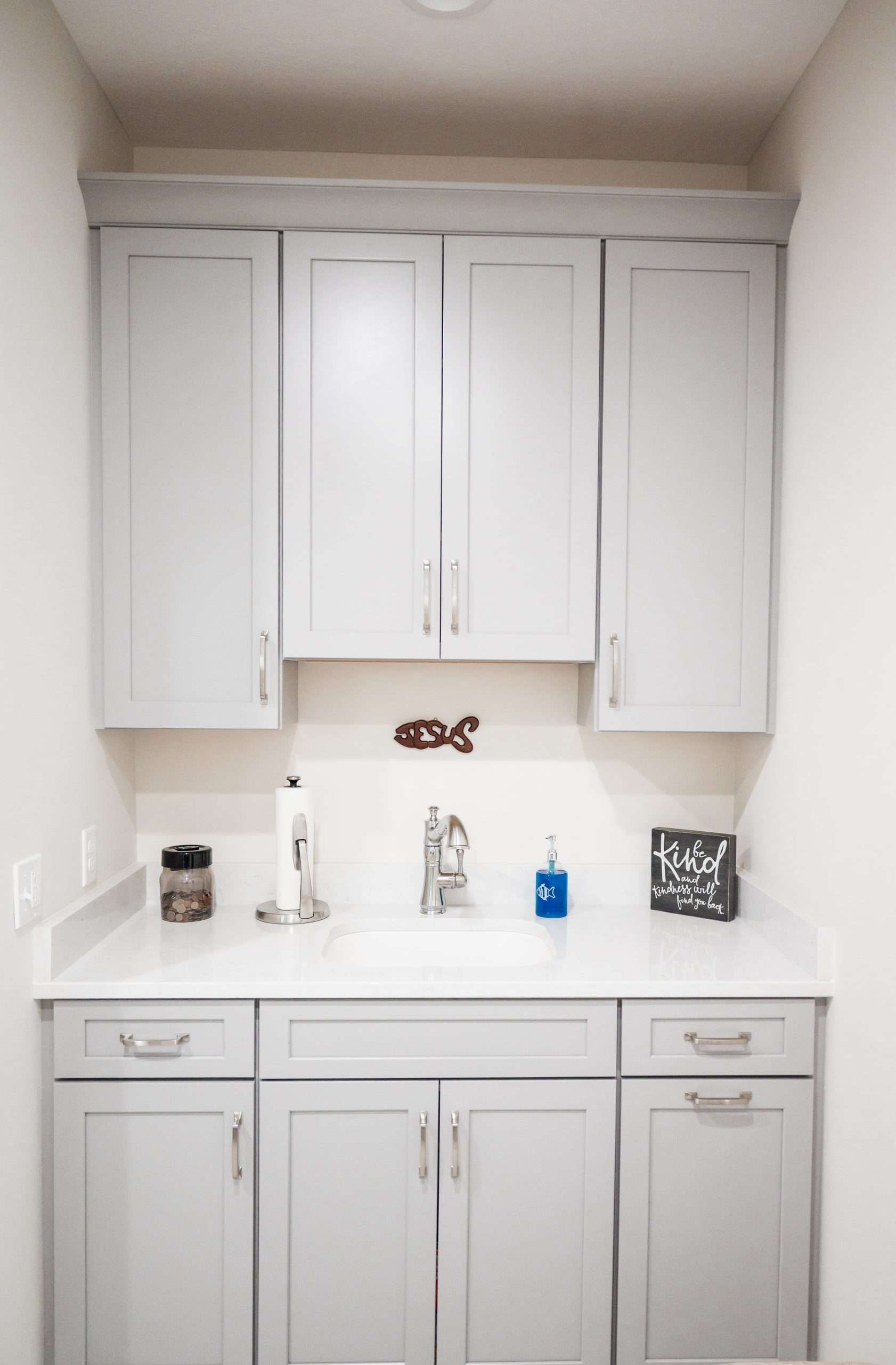White bathroom vanity with sink, mirror cabinet, and wall-mounted cabinets under a beige wall.