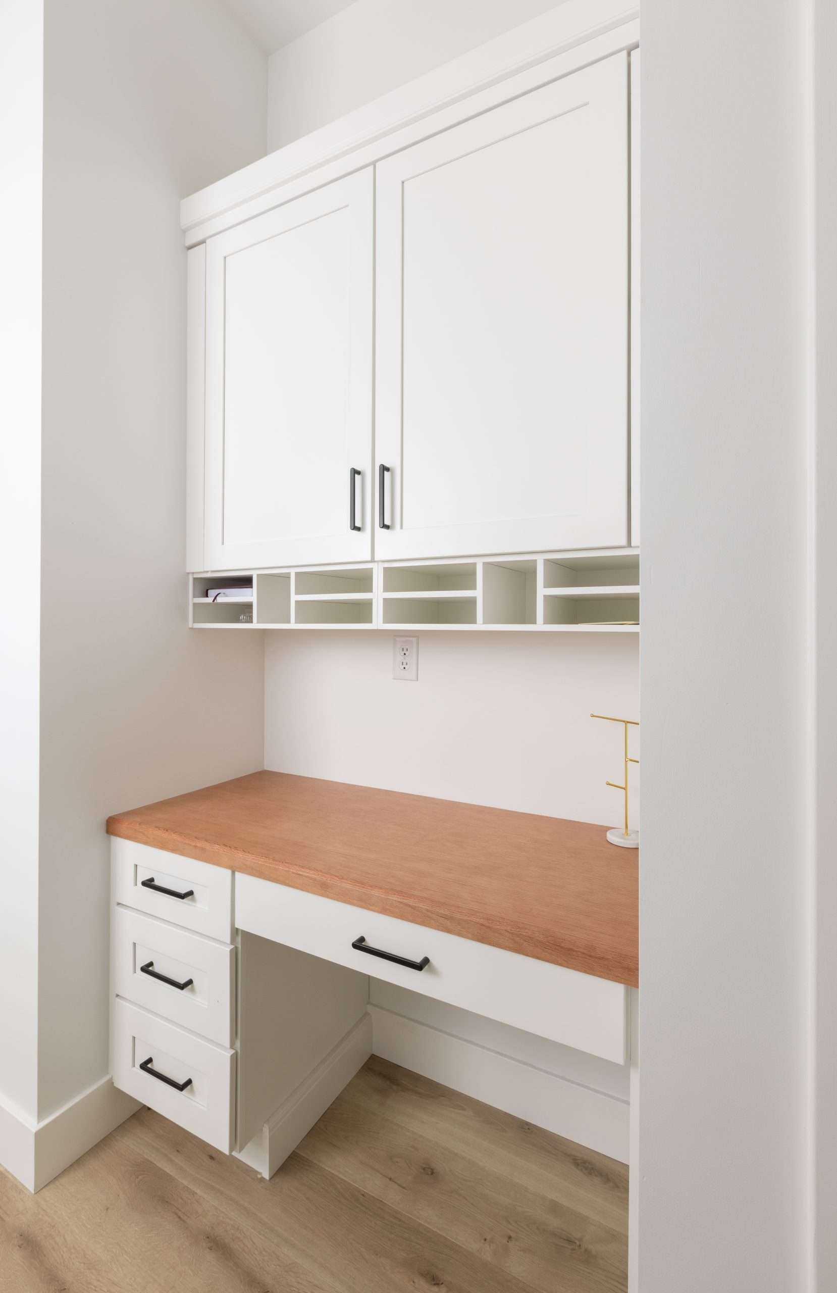 White built-in desk nook with upper cabinets, open cubbies, and a wood countertop in a bright room